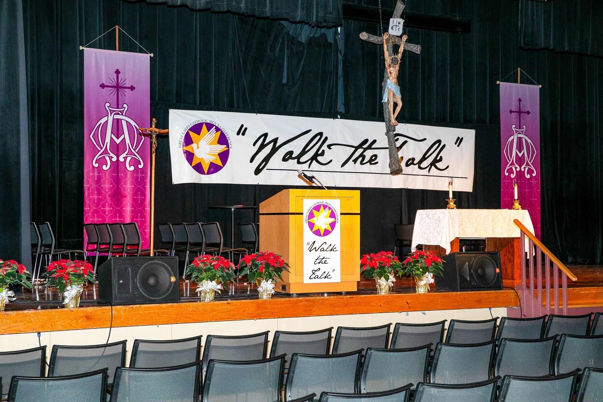 Church altar with cross, pulpit, and pink banners on a stage in front of empty seats