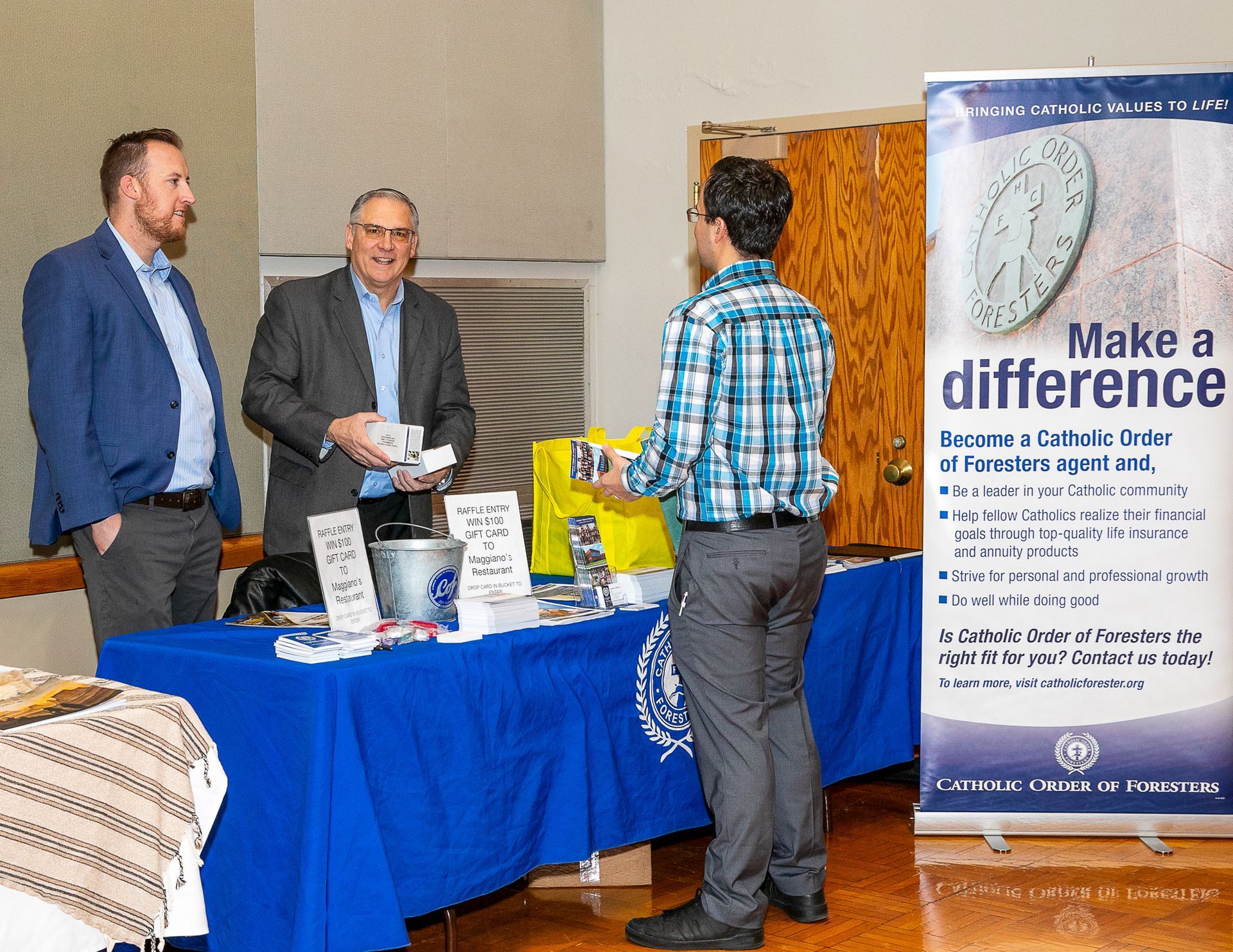 Three people at a blue table at a community outreach booth with a “Make a difference” banner.