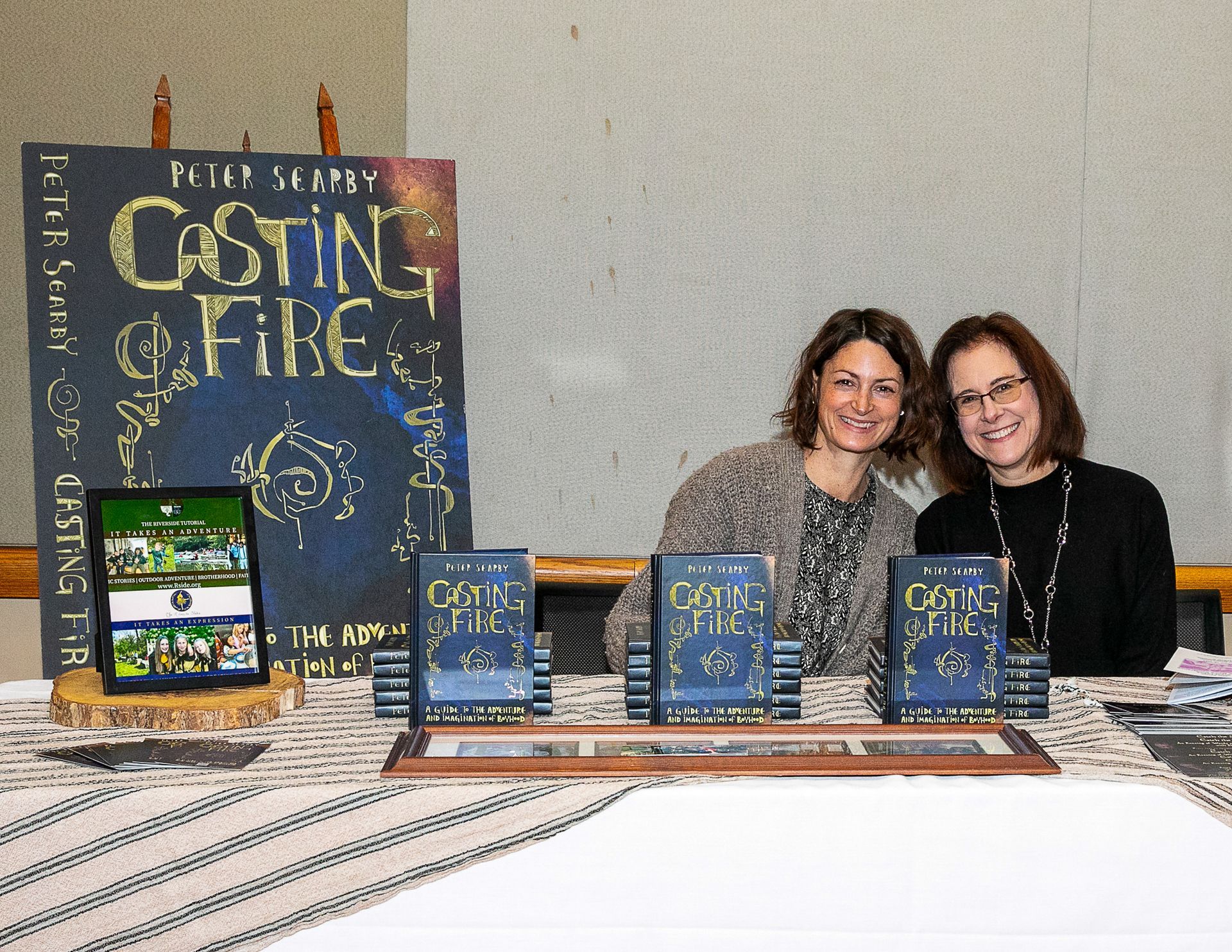 Book display at a table with two smiling people behind it and a large “Casting on Fire” poster.