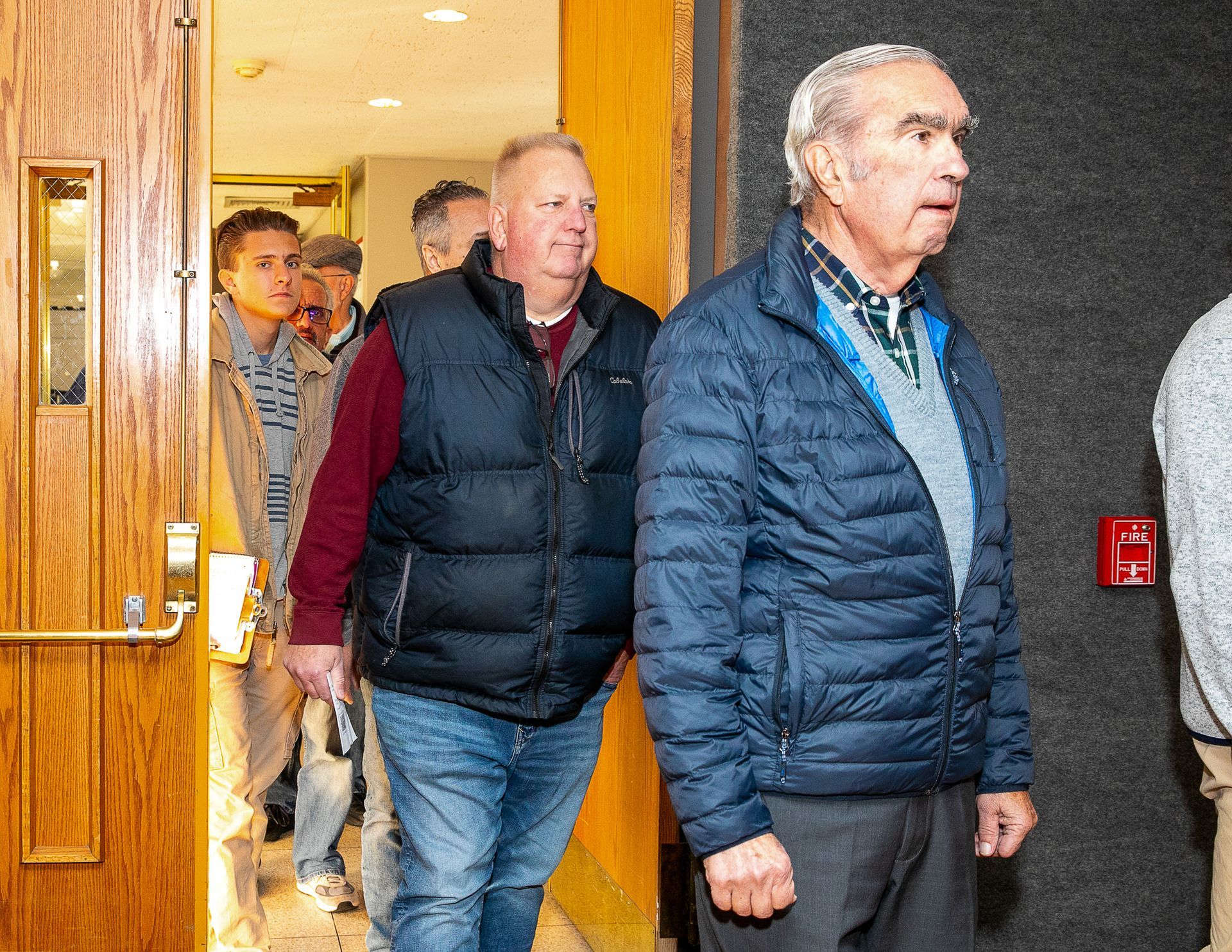 Two men in jackets walking through a doorway into a building hallway