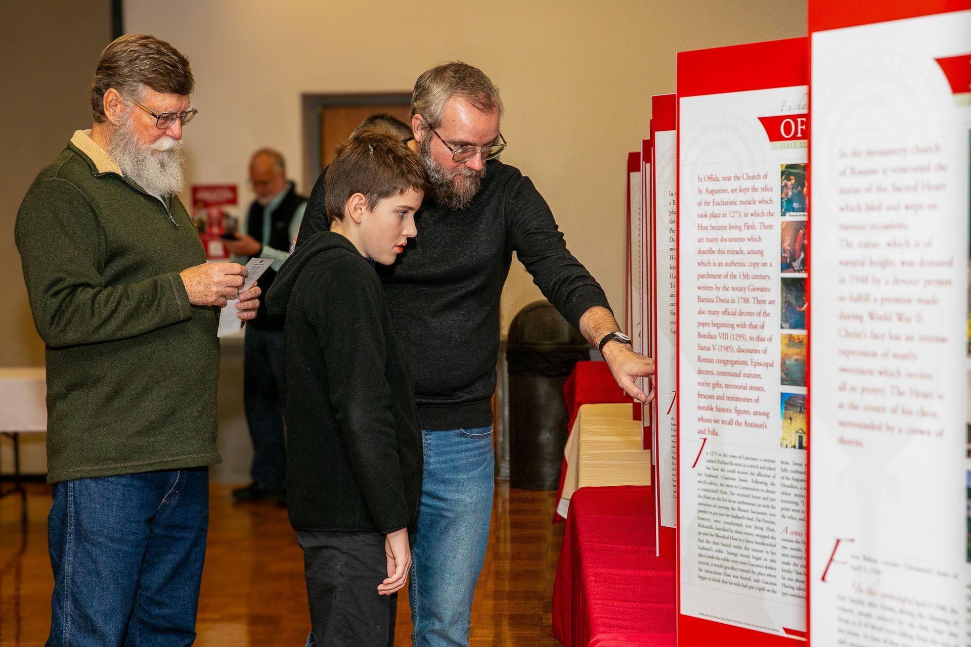 Three people reading display boards in a museum or gallery exhibit.