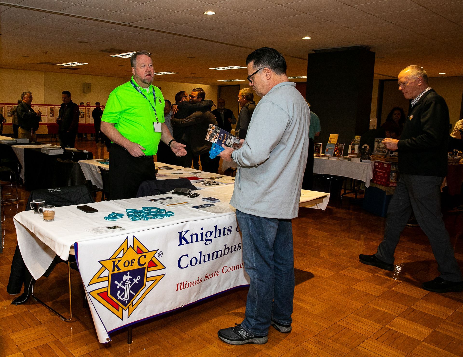 People at a Knights of Columbus table in a banquet hall, with brochures and a neon green shirt.