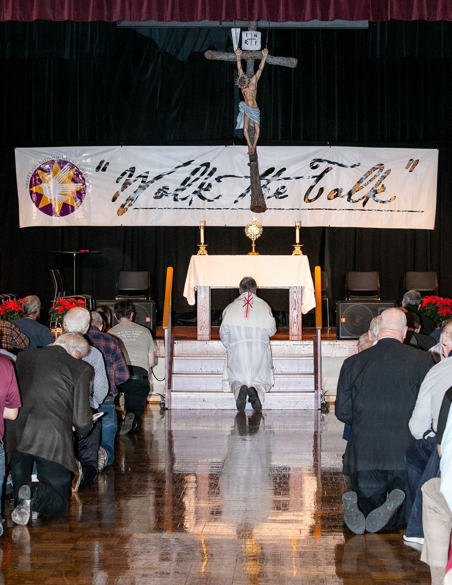 Congregation kneels in church before a crucifix and altar under a “Merry Christmas” banner.