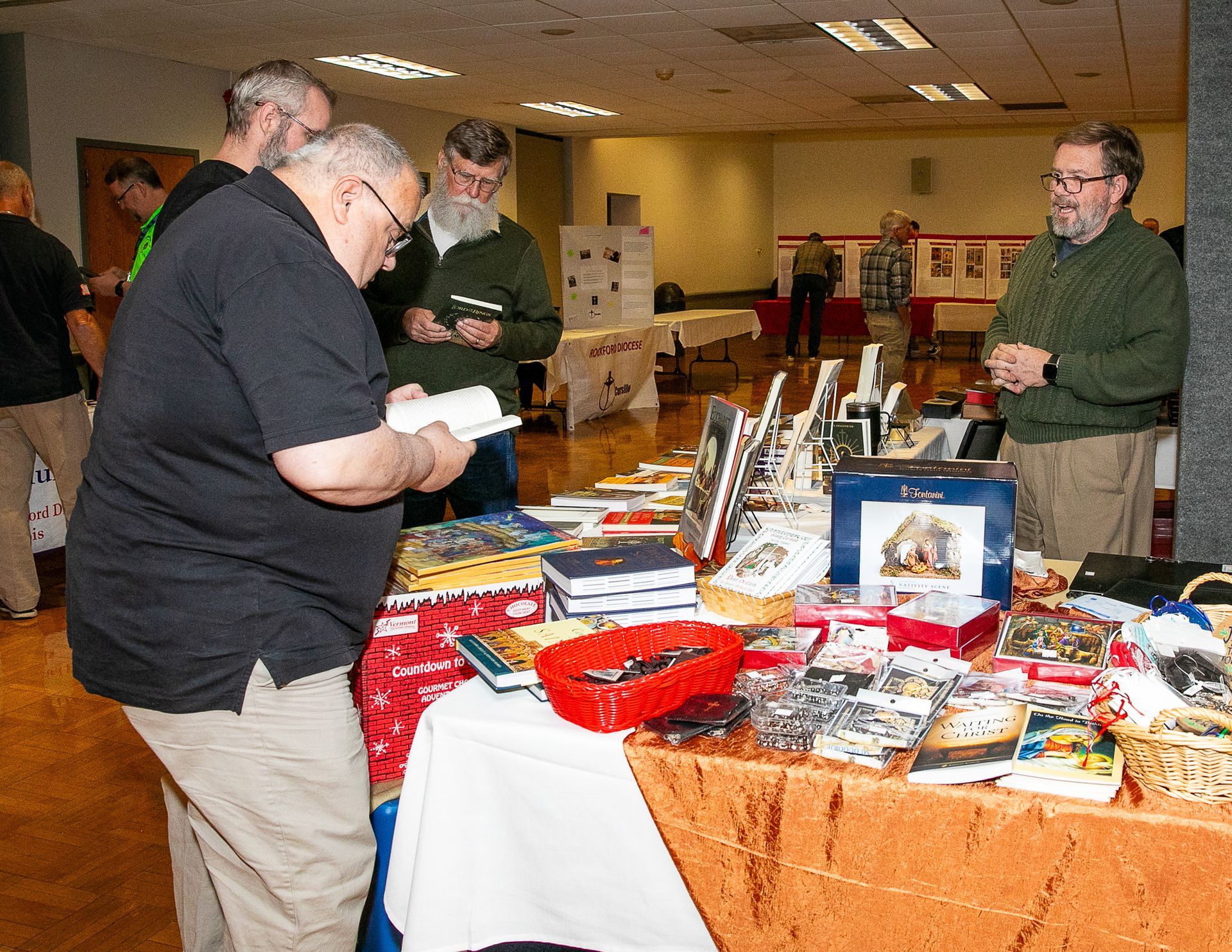People browsing a vendor table at an indoor craft fair with books, gifts, and small items.
