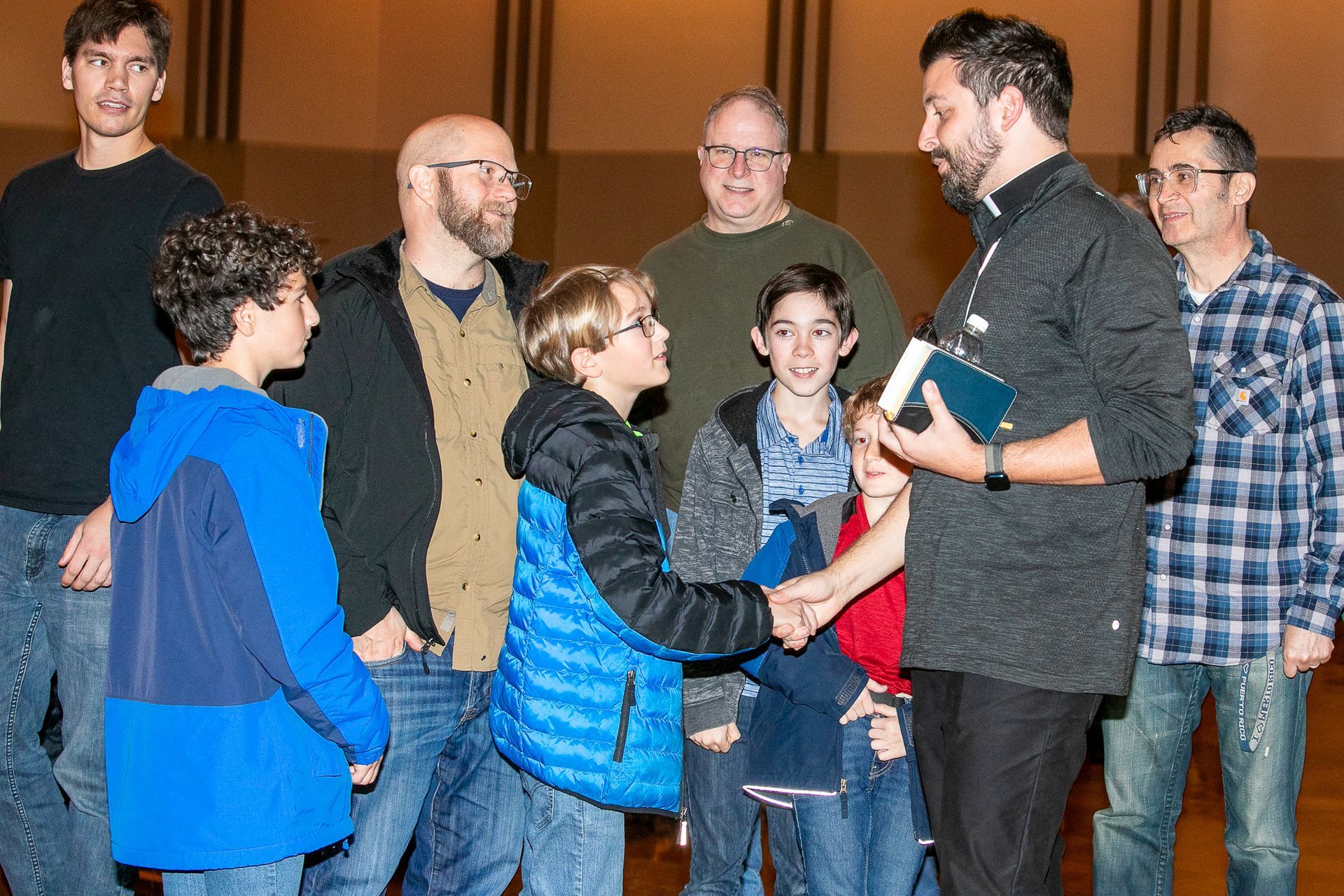 Group of people indoors, shaking hands and talking during a casual gathering.