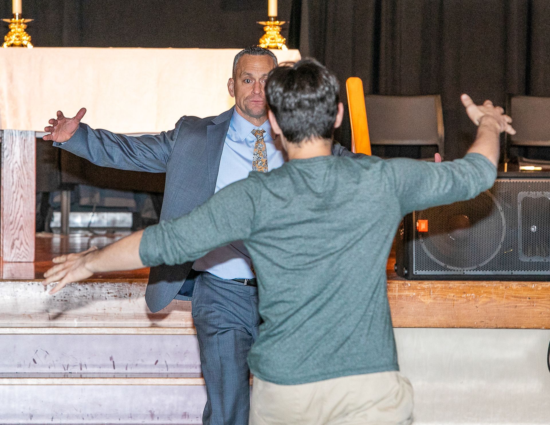 Two people with outstretched arms facing each other in a dim indoor room