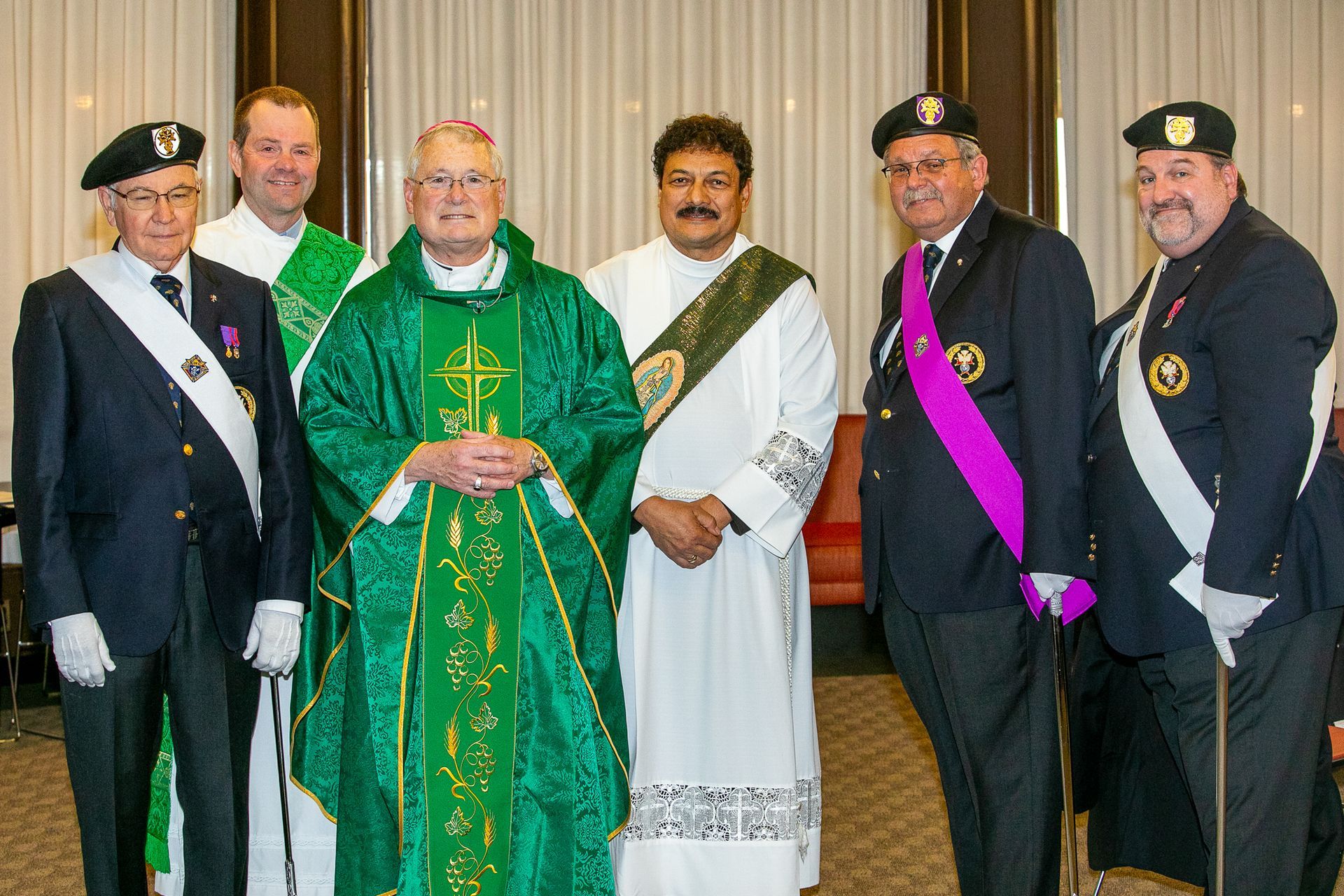 Five men in formal uniforms and clerical robes standing together indoors at a ceremony
