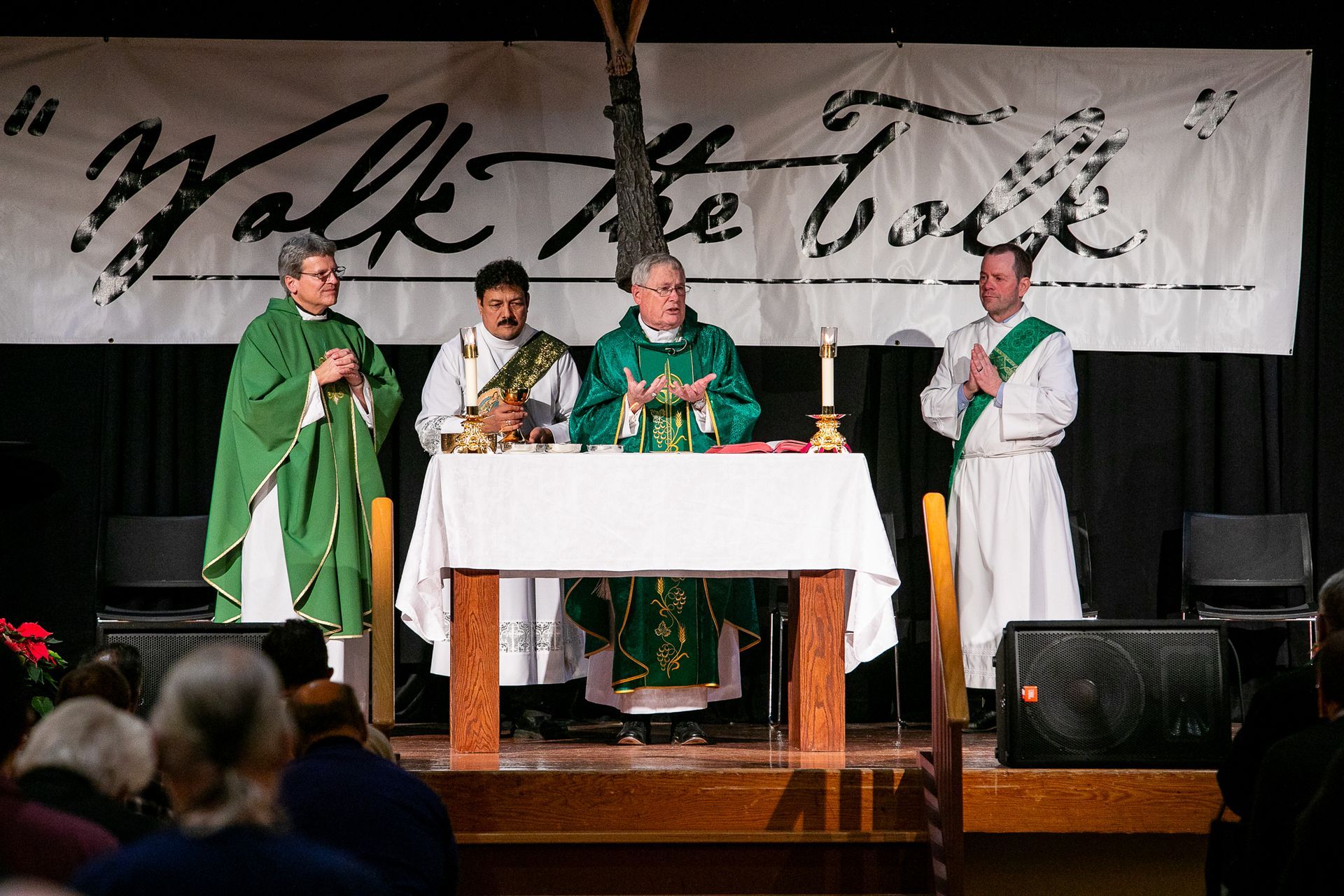 Four clergy in green and white vestments stand at a church altar during a service