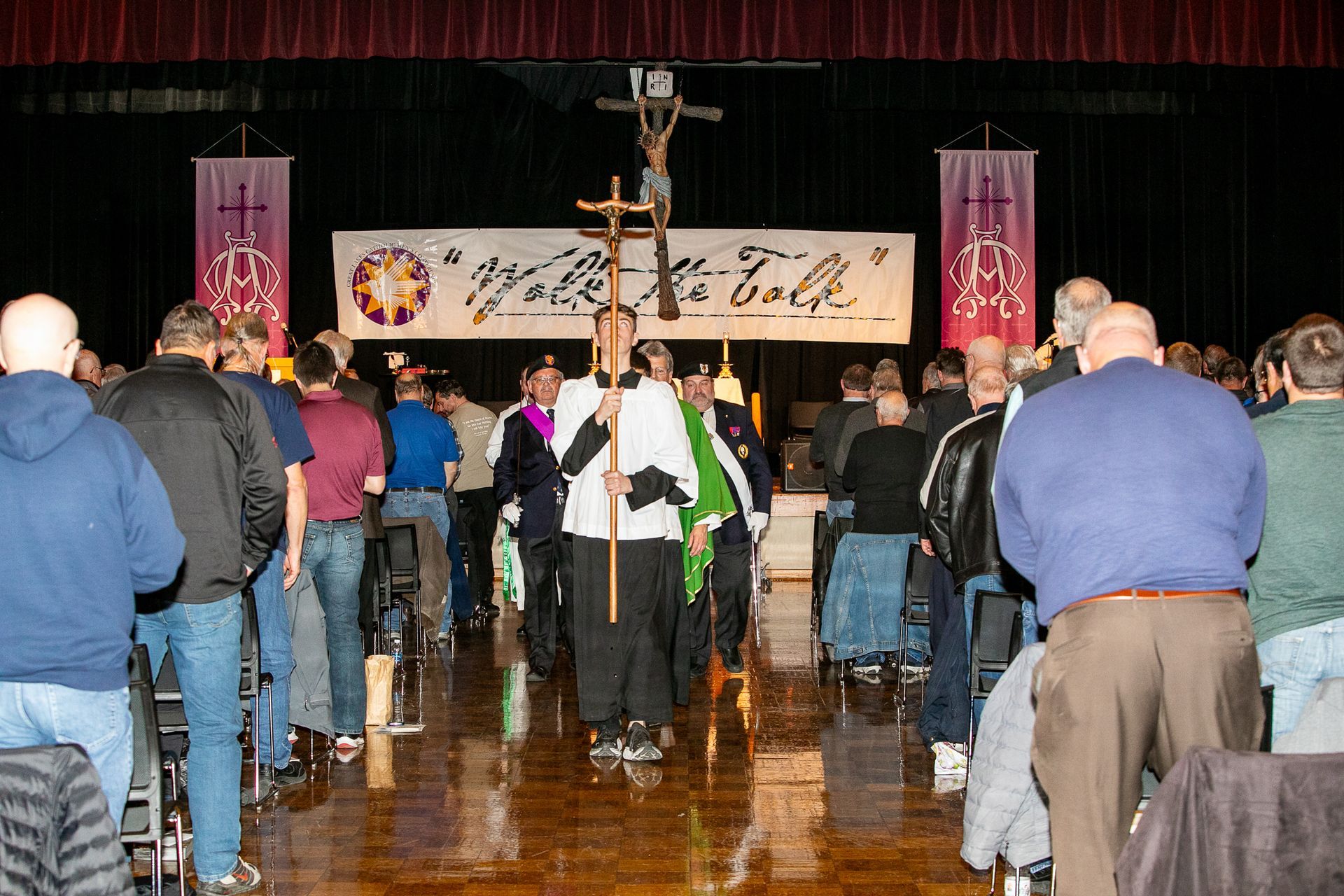 People gathered in a hall facing a stage with banners and a large cross.