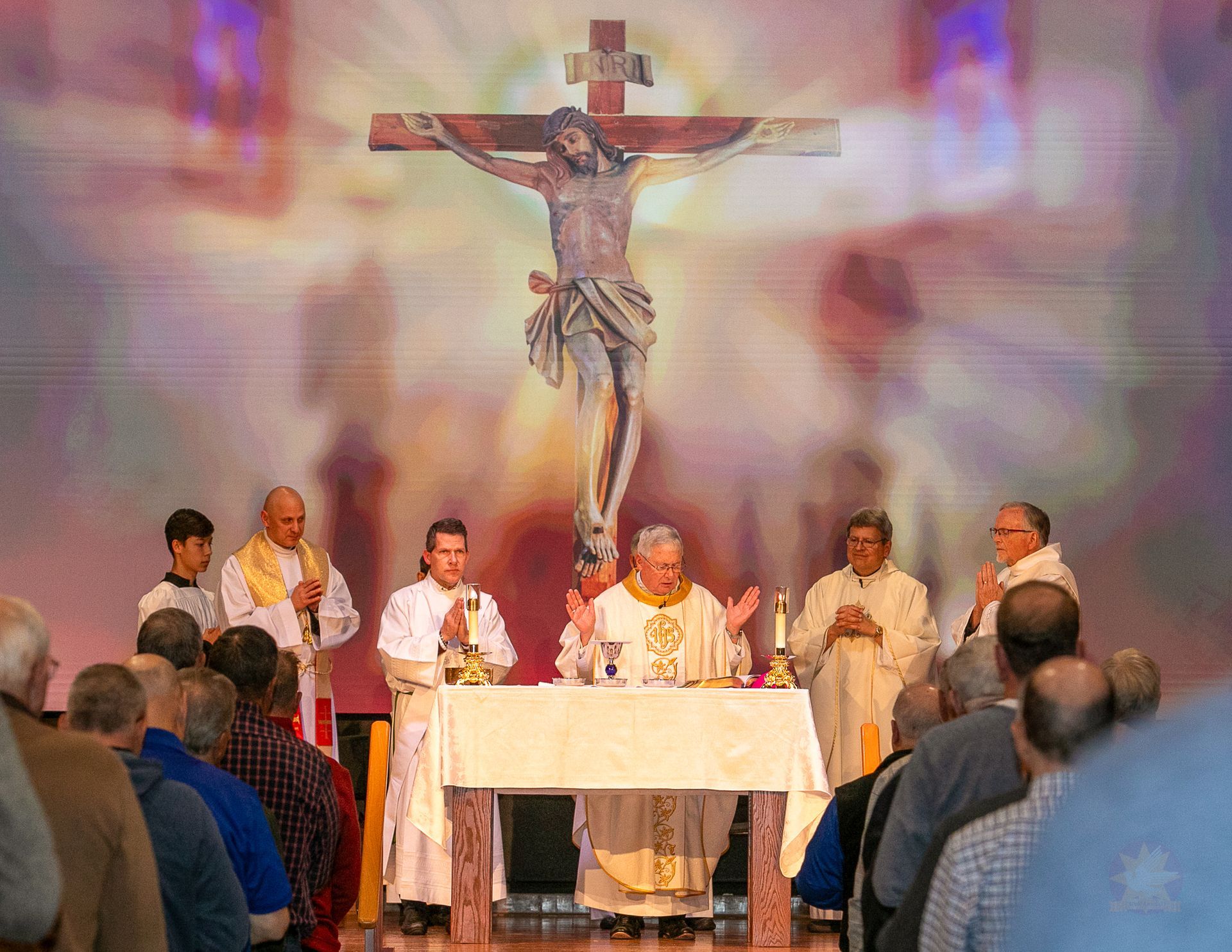 Priests celebrating Mass at an altar beneath a large crucifix in a church