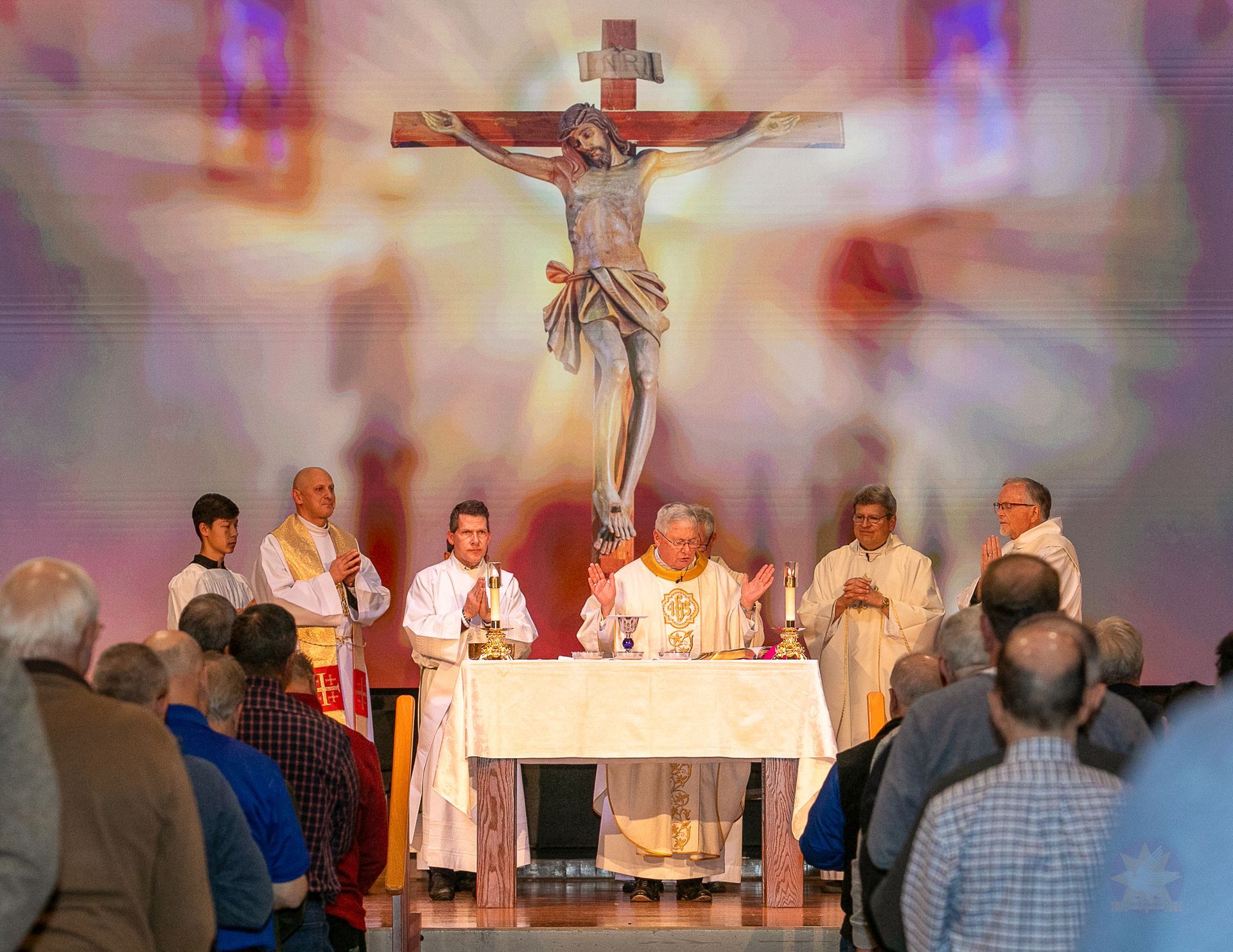Catholic mass at an altar beneath a crucifix, with priests and congregants in a church
