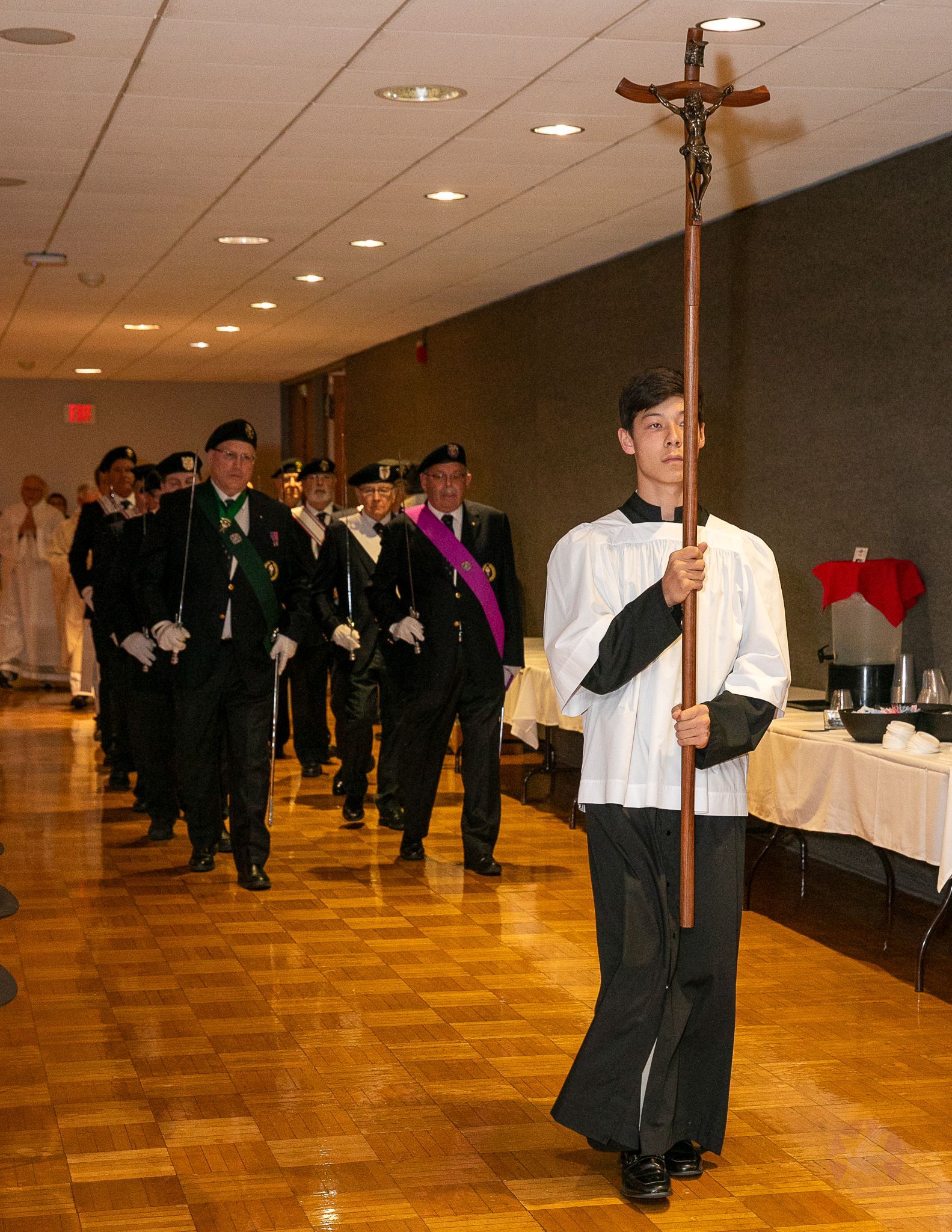A man carries a tall ceremonial crucifix while a group follows at a Catholic men's conference.