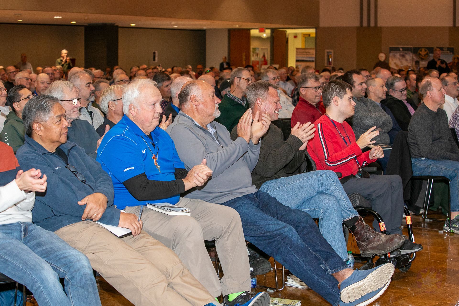 Audience seated in a conference hall, applauding during a Catholic men's conference.