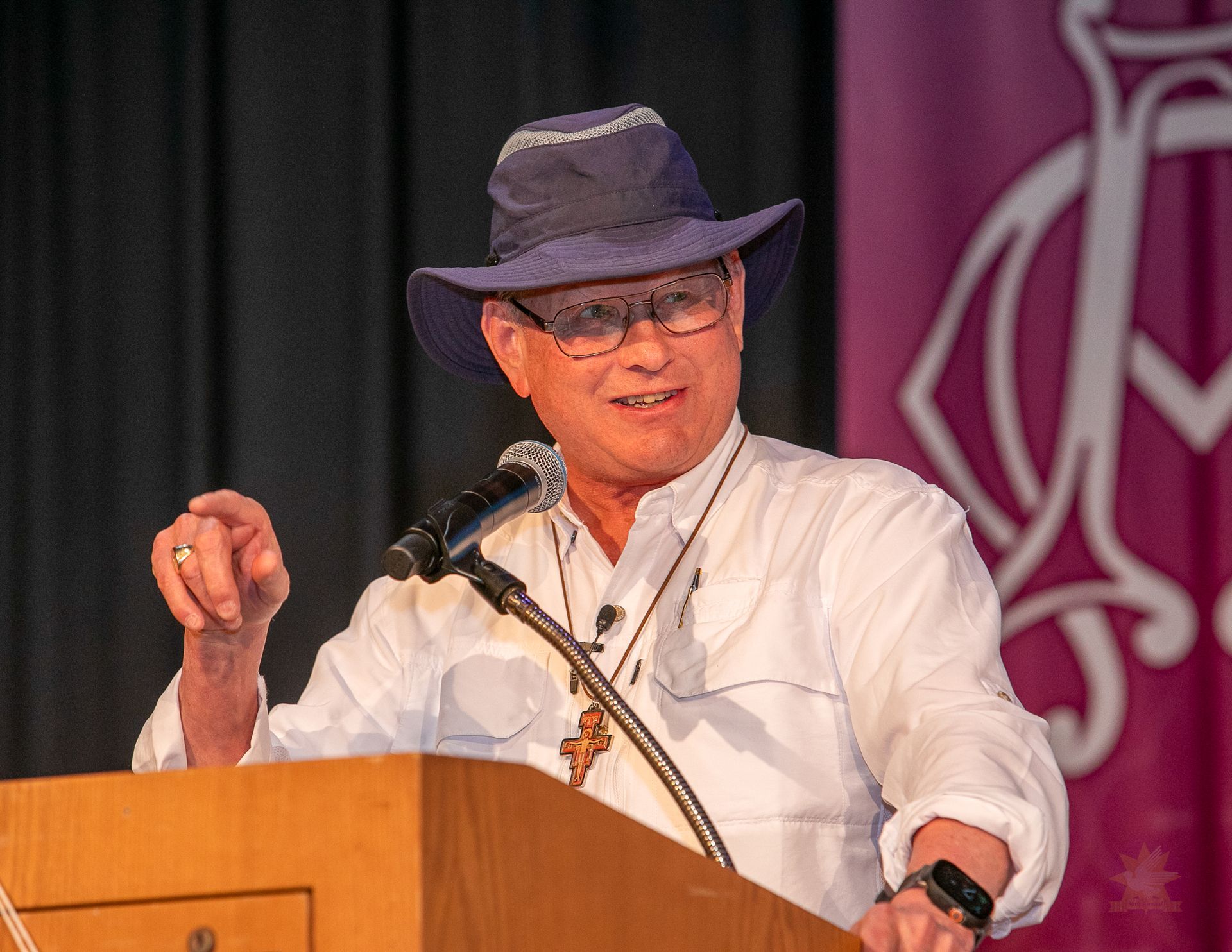 Steve Ray speaking at a podium on stage, wearing a white shirt and glasses