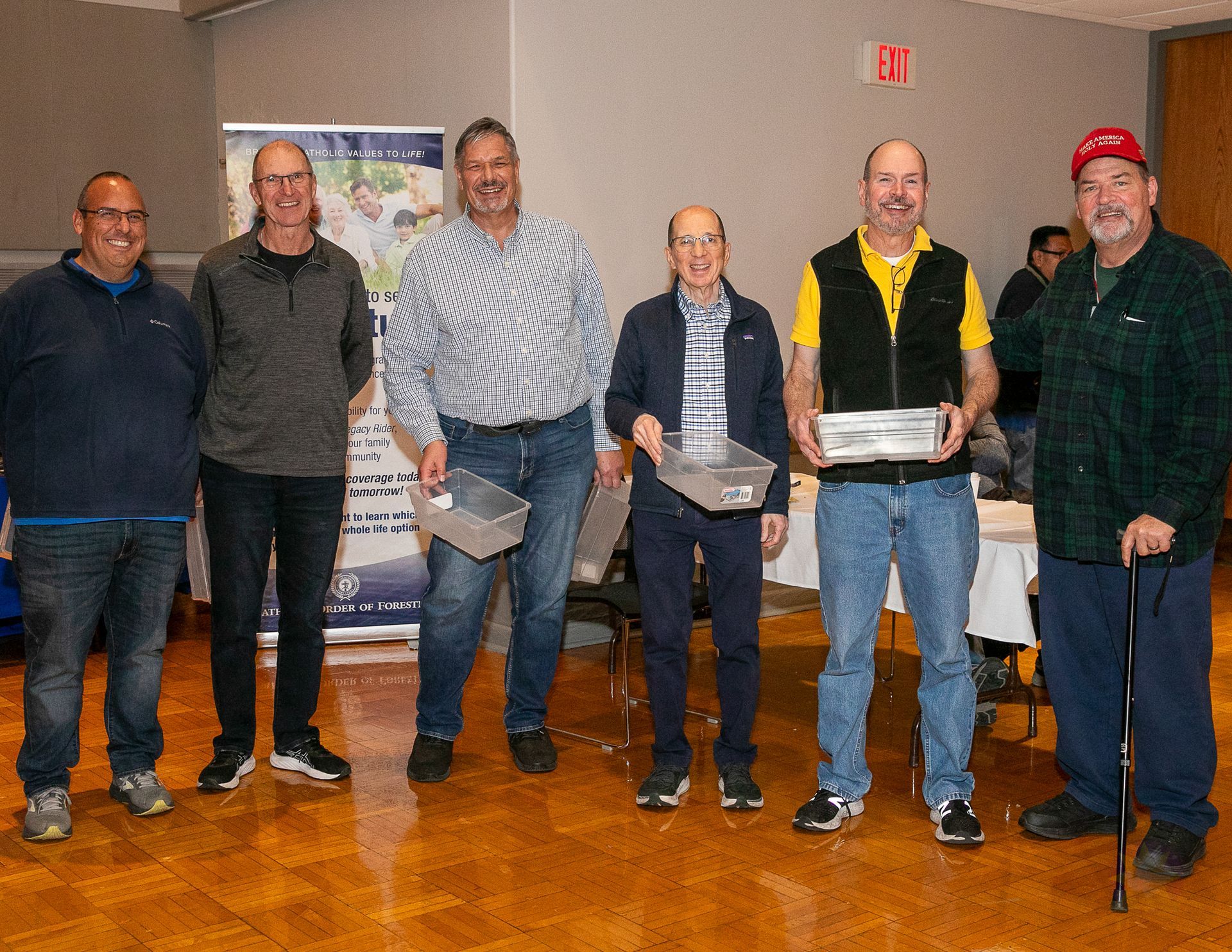 Six people standing indoors at an event, posing in front of a table with papers and trophies.