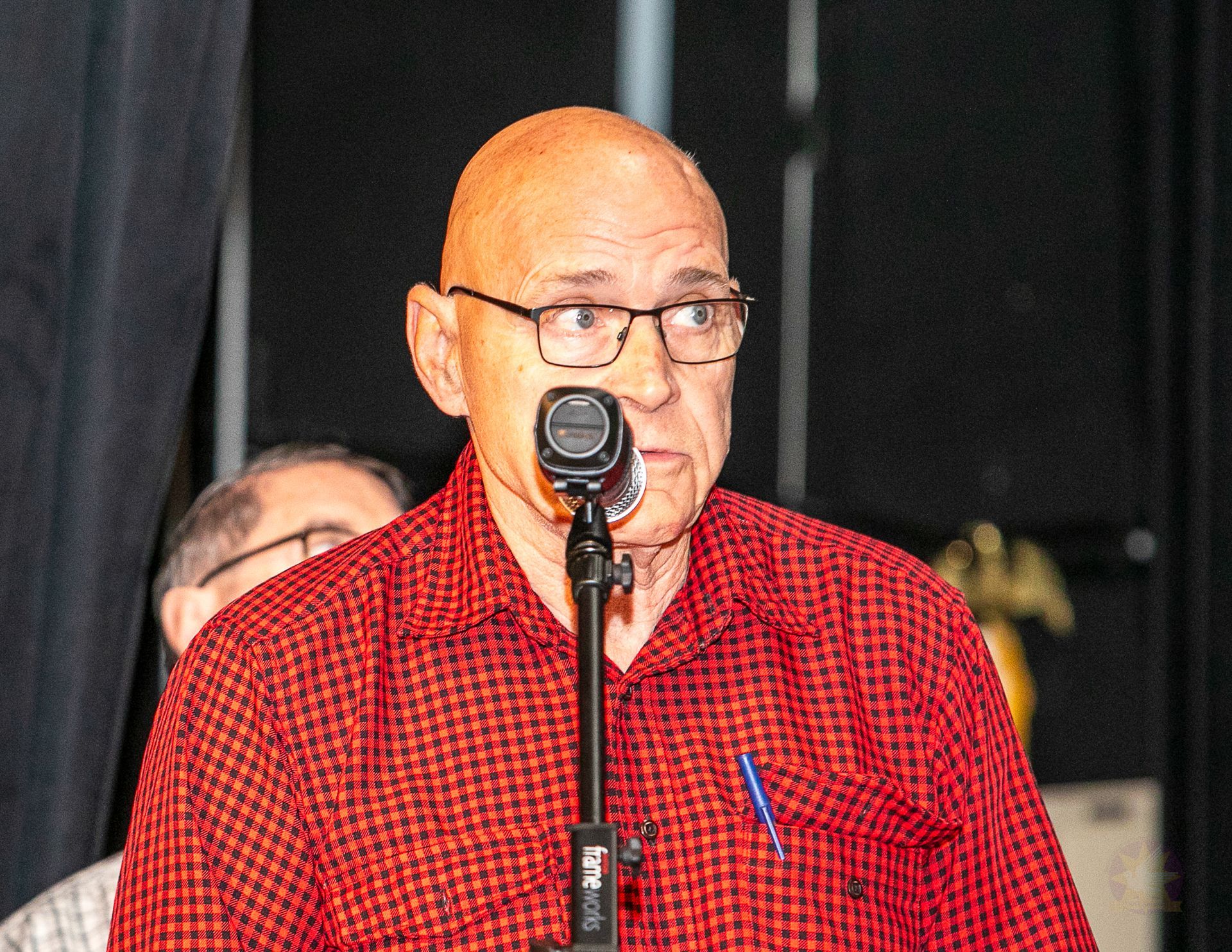 Man speaking at a microphone in a red shirt on a stage