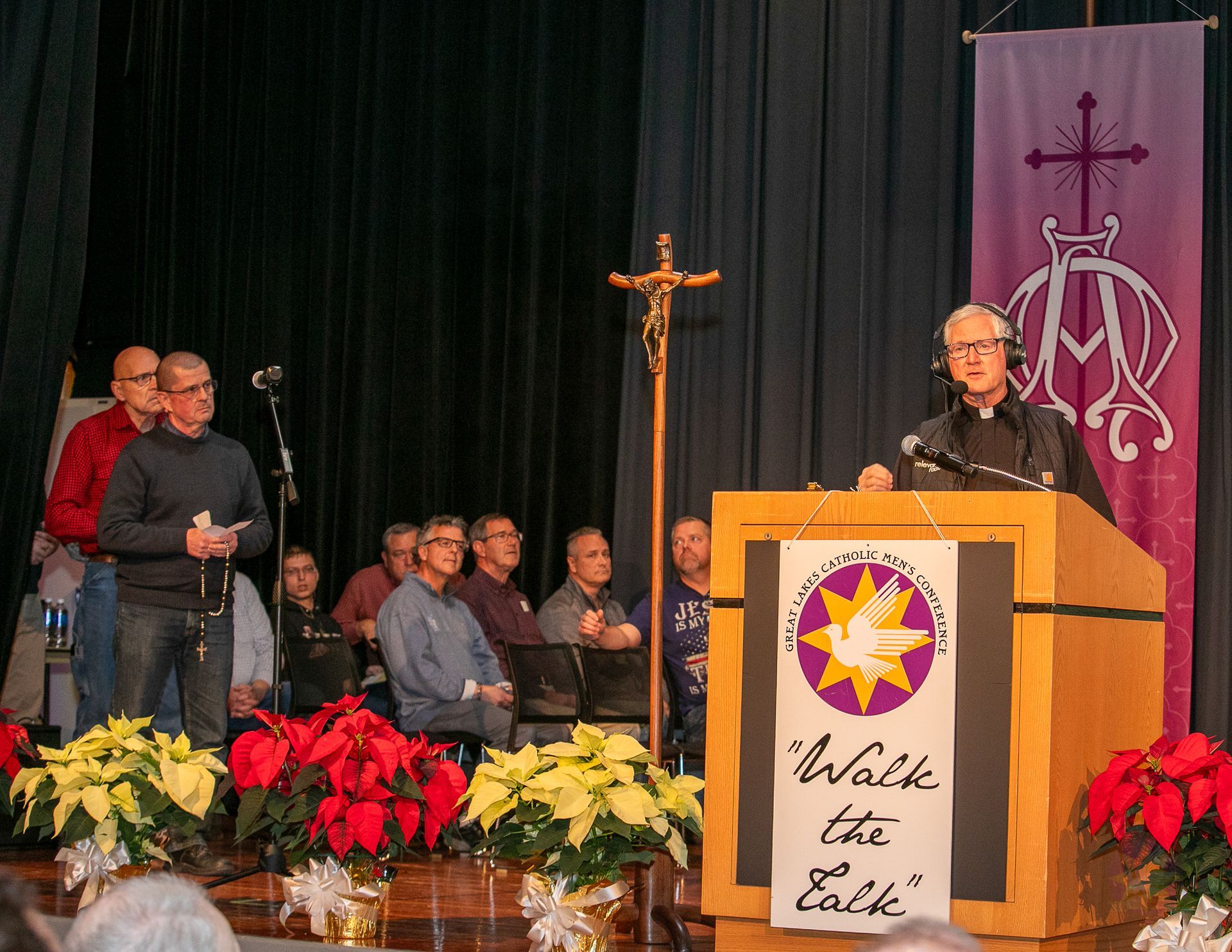 Speaker at podium on stage with cross, seated audience, and poinsettias during a church event