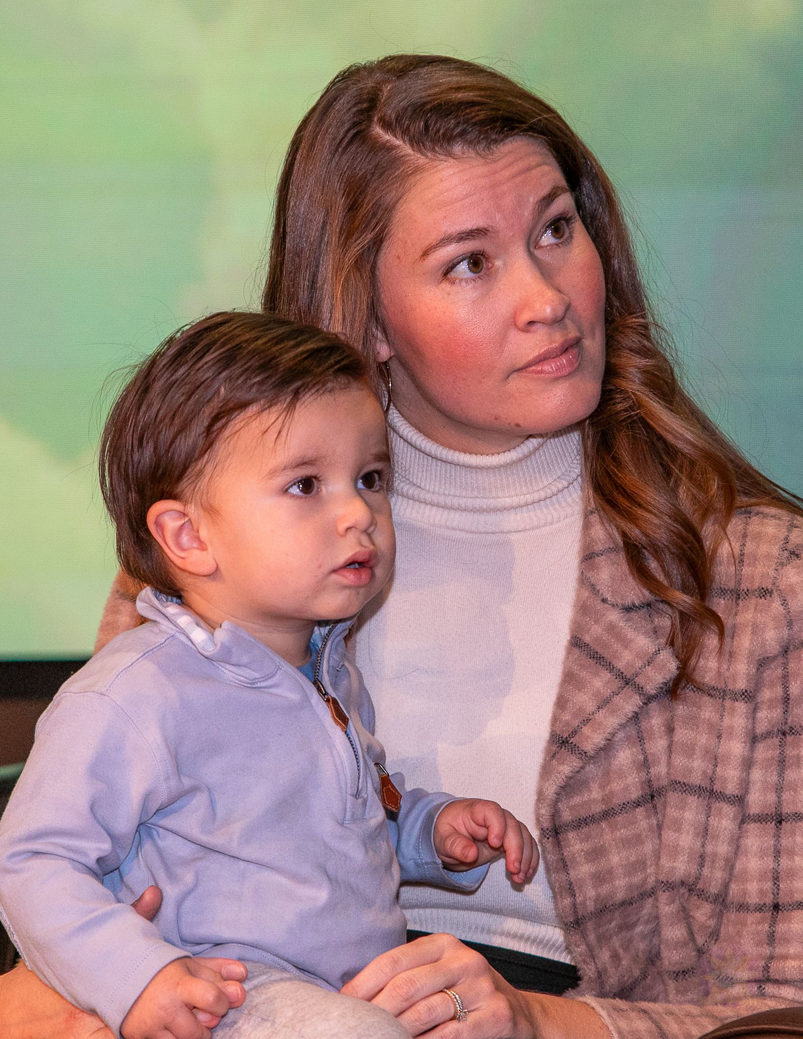 Woman holding a toddler against a green background, both looking off to the side.