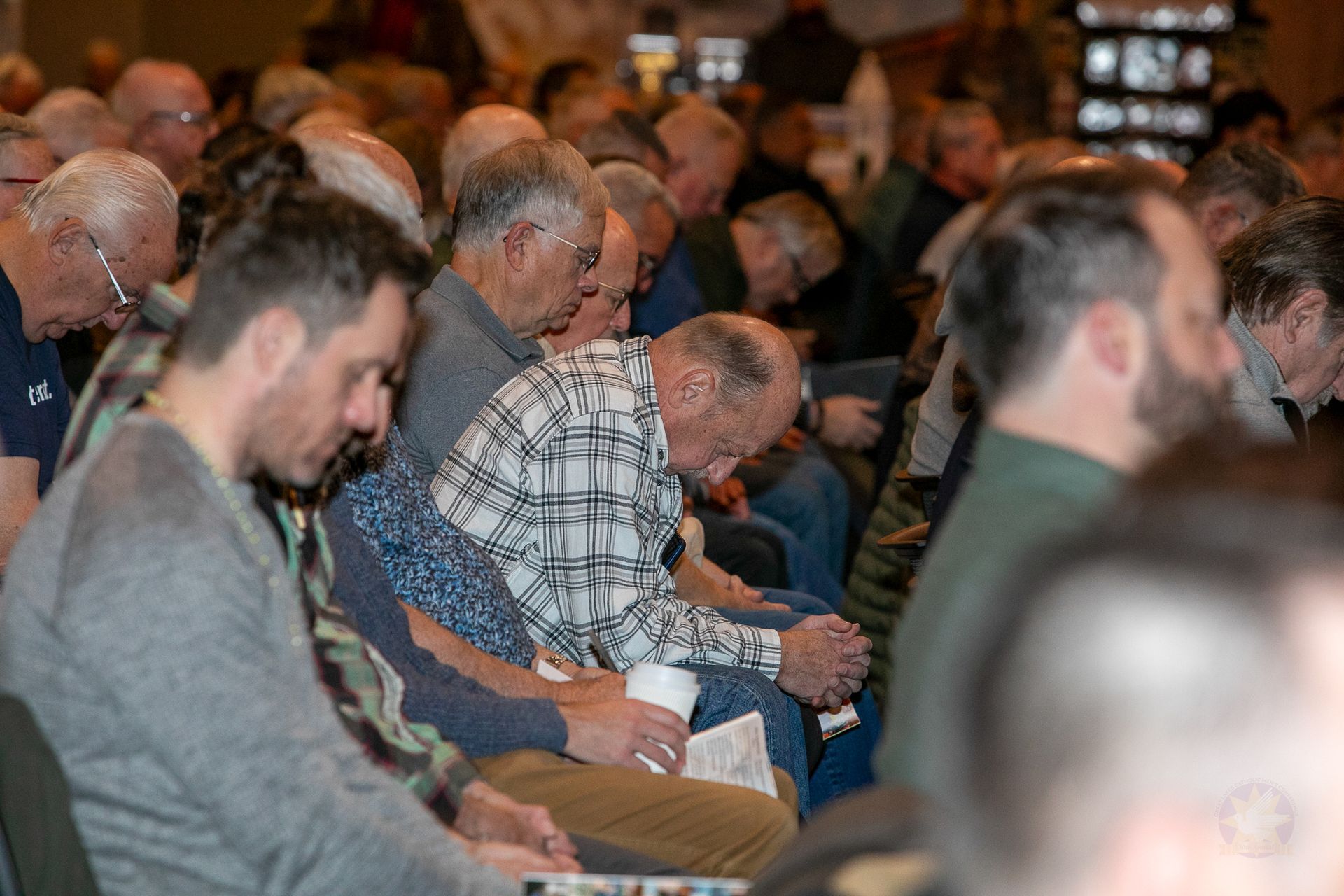 Audience seated and listening at a Catholic men's conference, with people taking notes in the foreground.