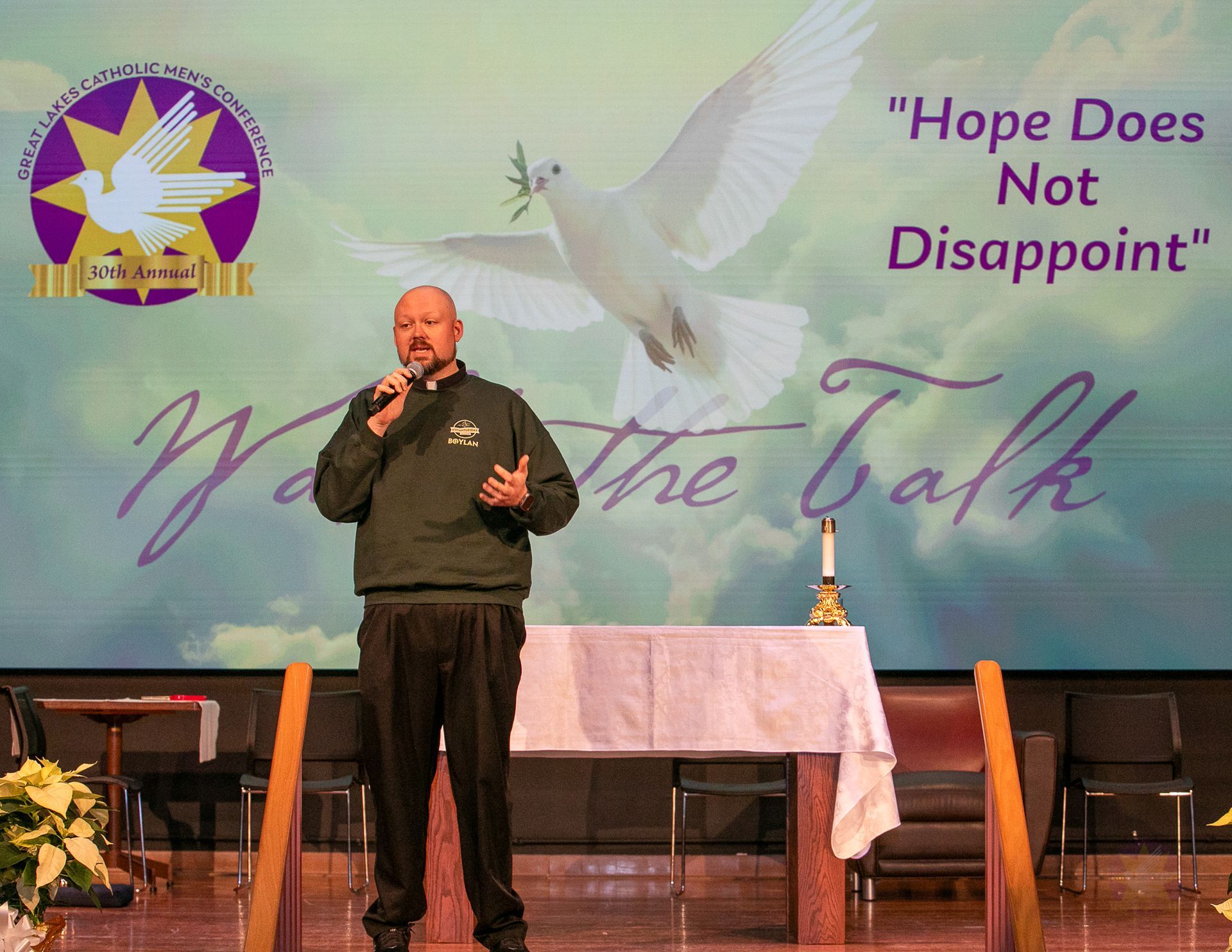 Rev. Robert Blood on a stage in front of banner reading “Hope Does Not Disappoint” and “Walk the Talk”
