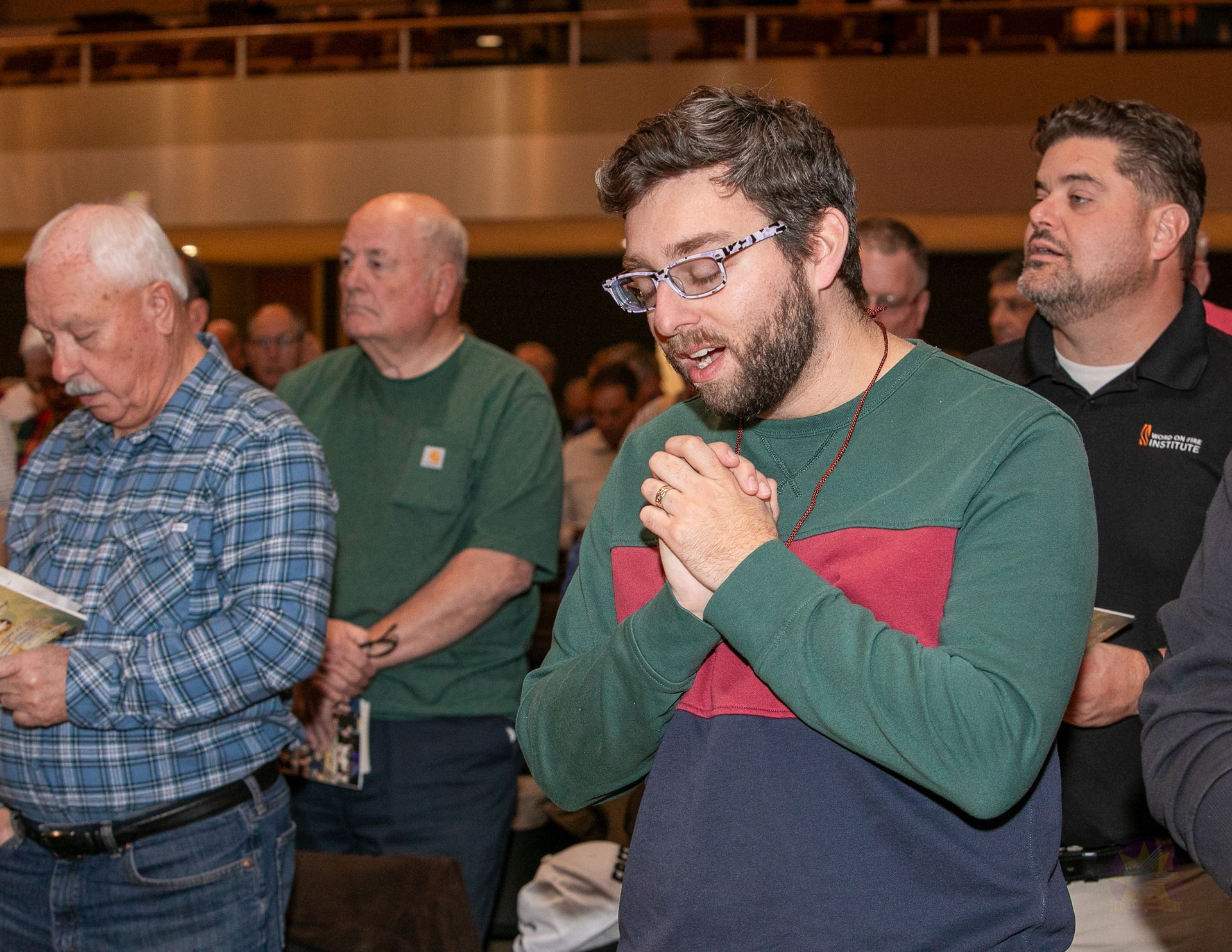 People standing indoors with hands clasped, one reading from a paper in the foreground.