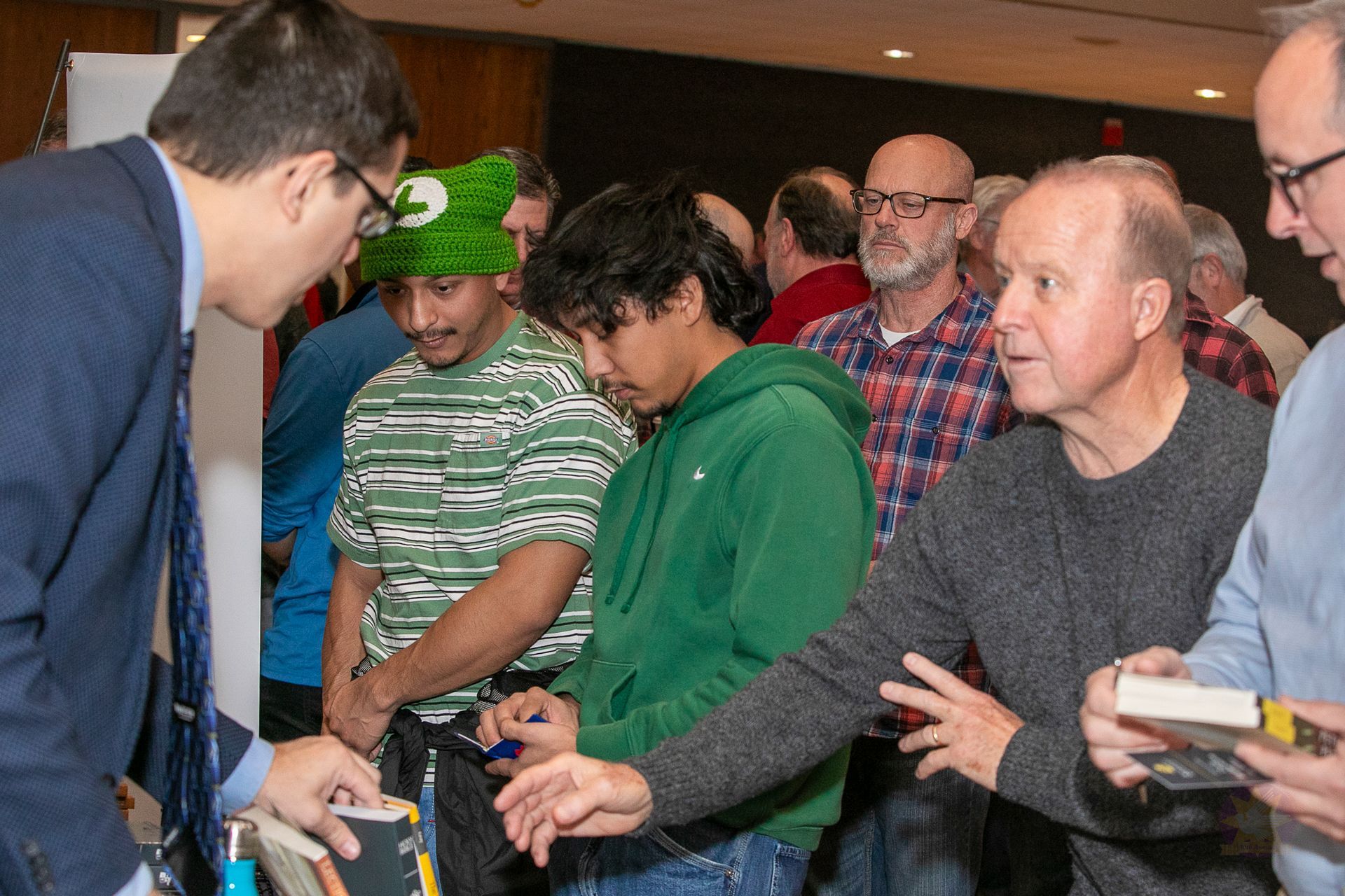 People in a crowd reach toward a man handing out items at a table.