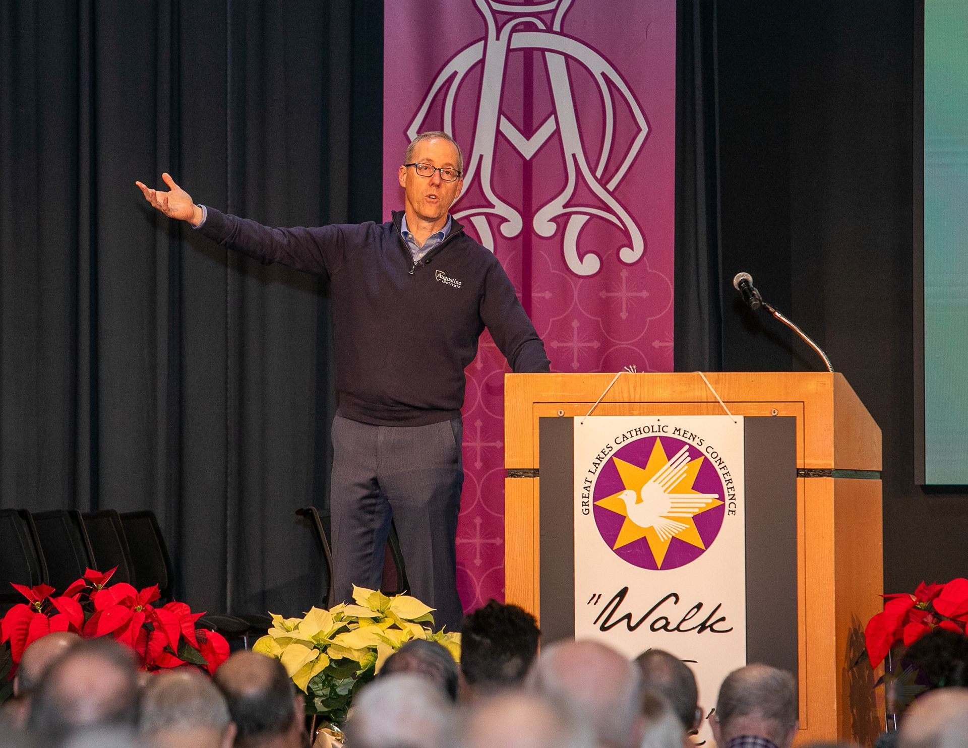 Dr. Tim GRay at podium on stage, gesturing beside a microphone, with audience in foreground.