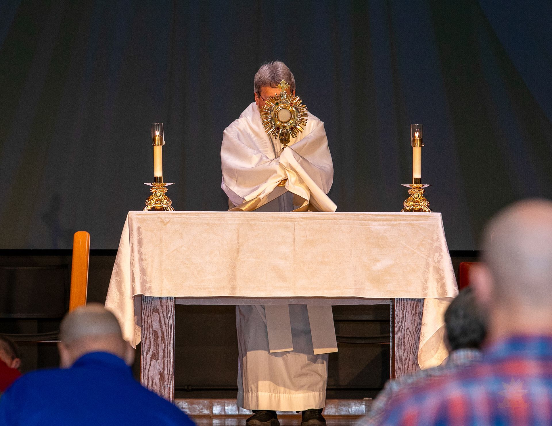Priest standing behind a church altar with candles, holding a monstrance during a service
