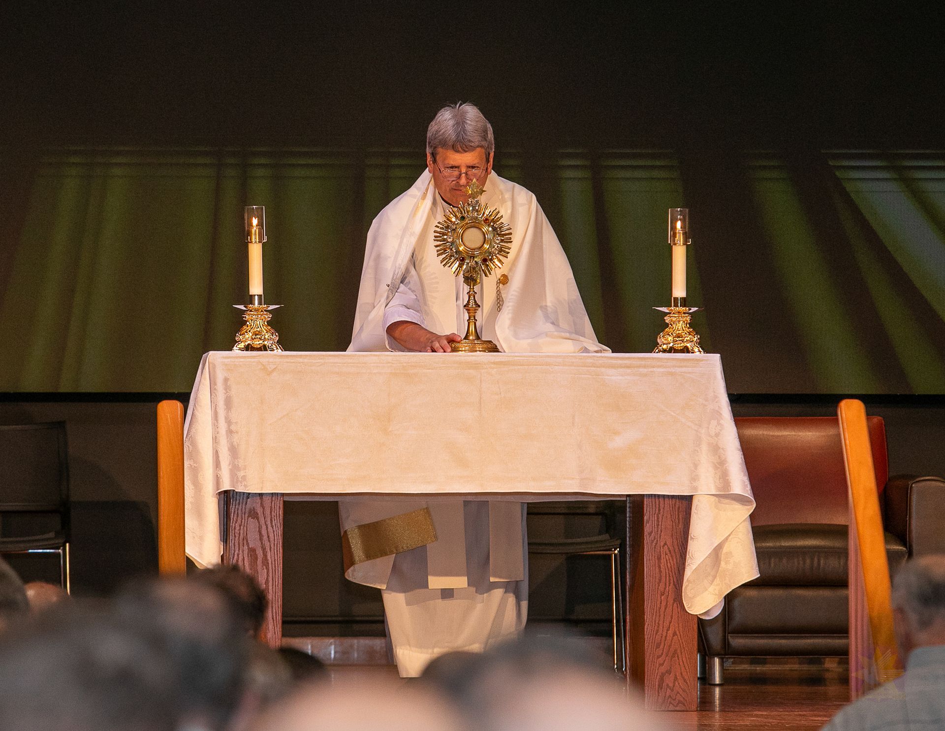 Priest standing at an altar with candles, reading during a church service