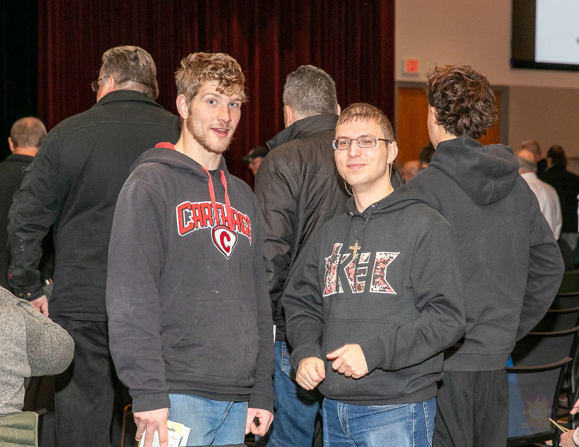 Three people in dark hoodies standing indoors at a crowded event.