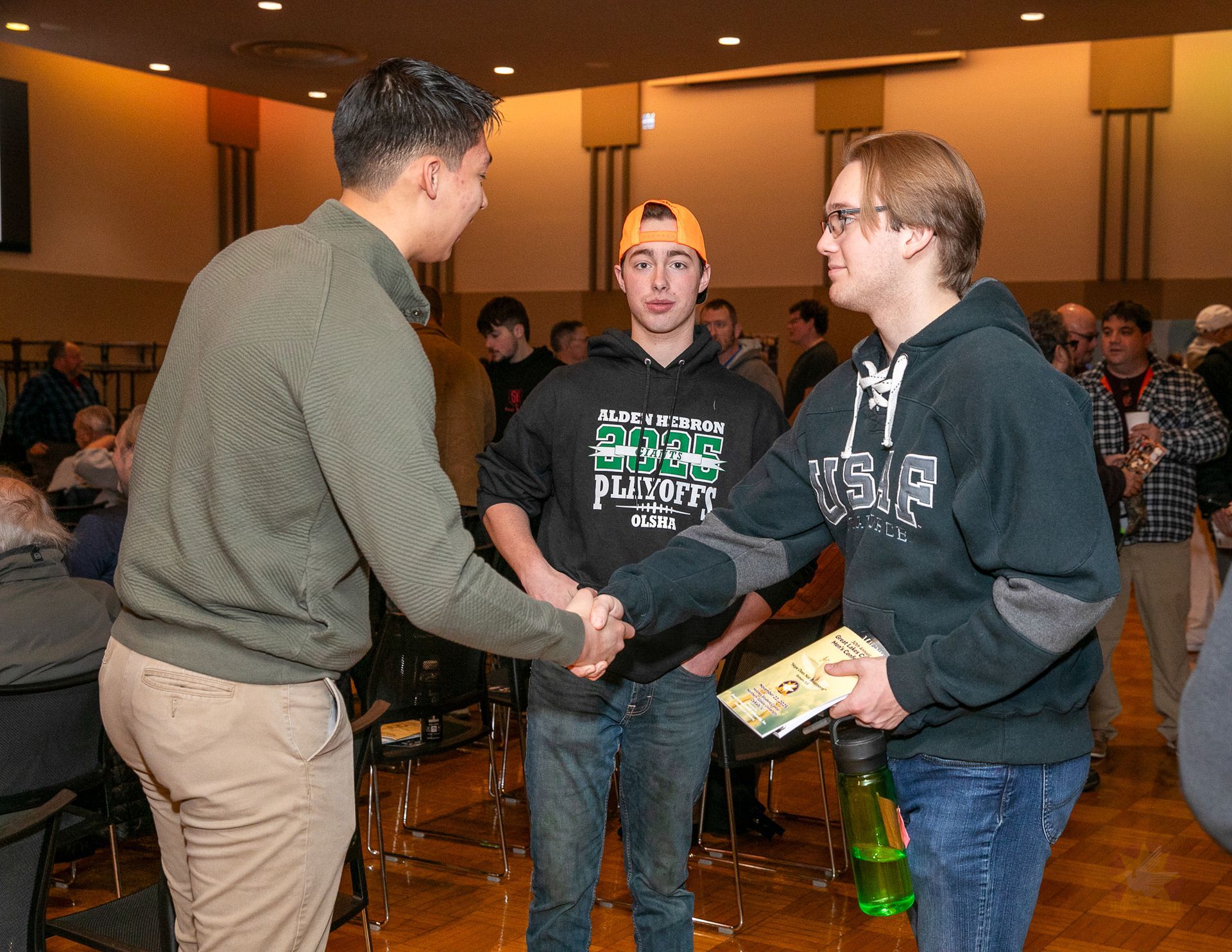 Two people shaking hands at an indoor event, with a third person holding a small box nearby.
