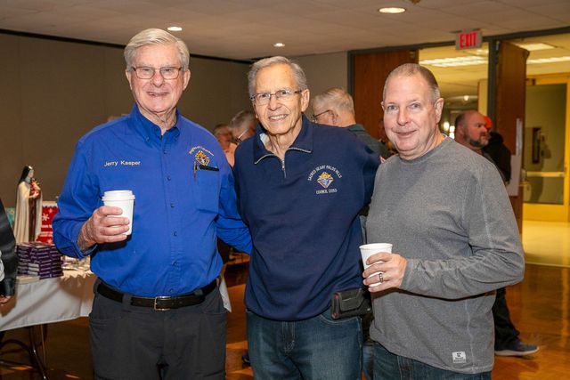 Three men holding cups at an indoor gathering, standing together and smiling.