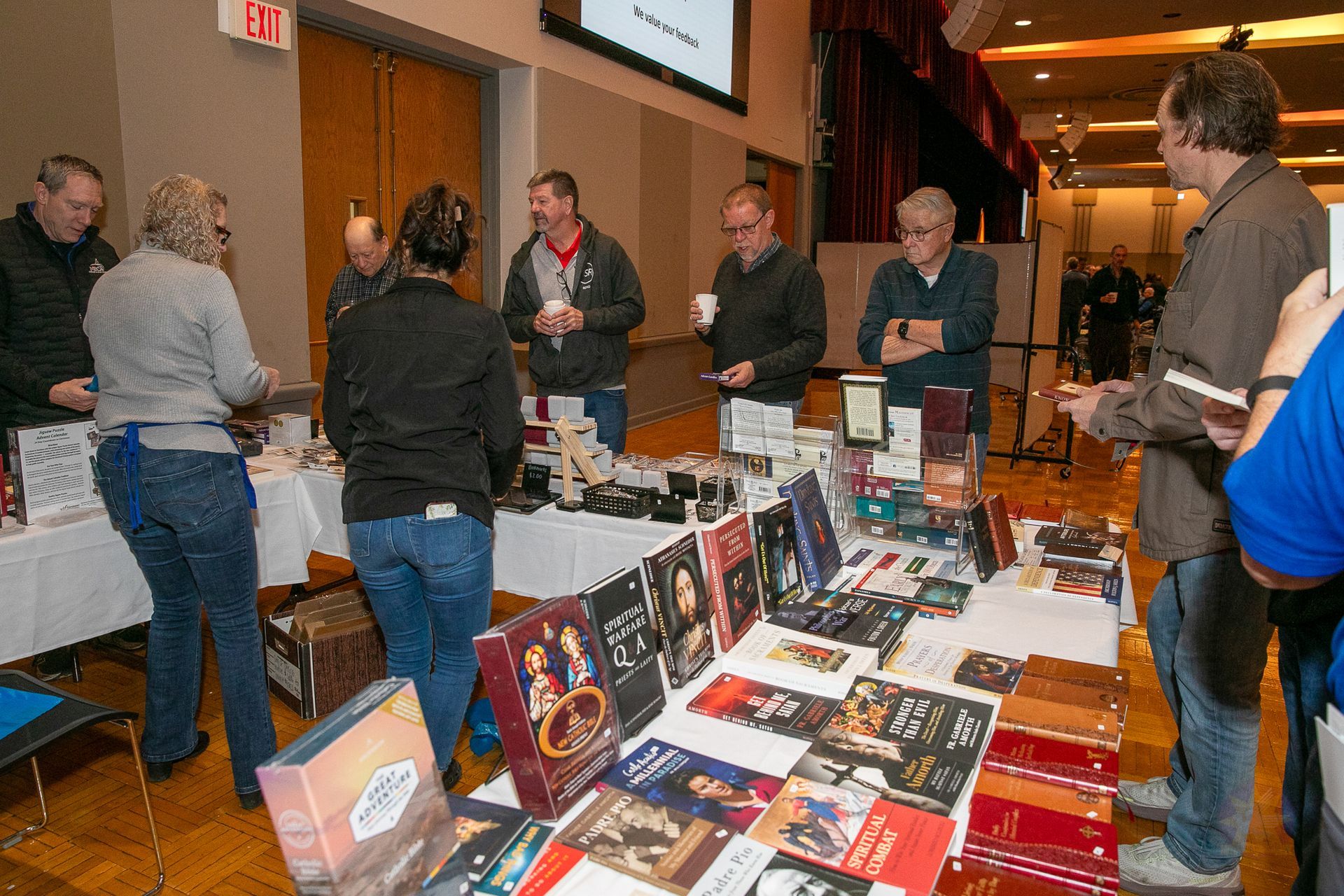 People browsing books at a table display in a busy indoor event hall