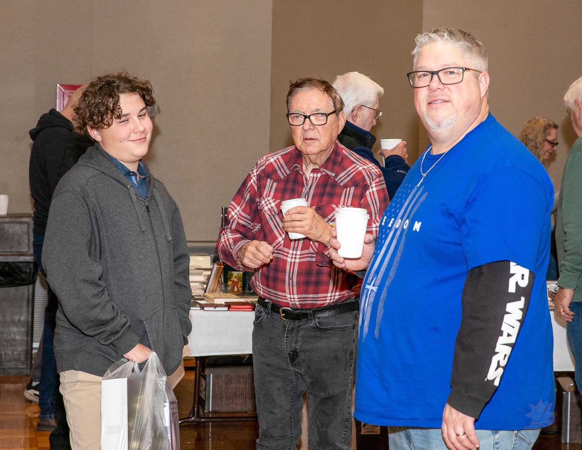 Three people standing indoors at a social event, holding drinks and chatting.