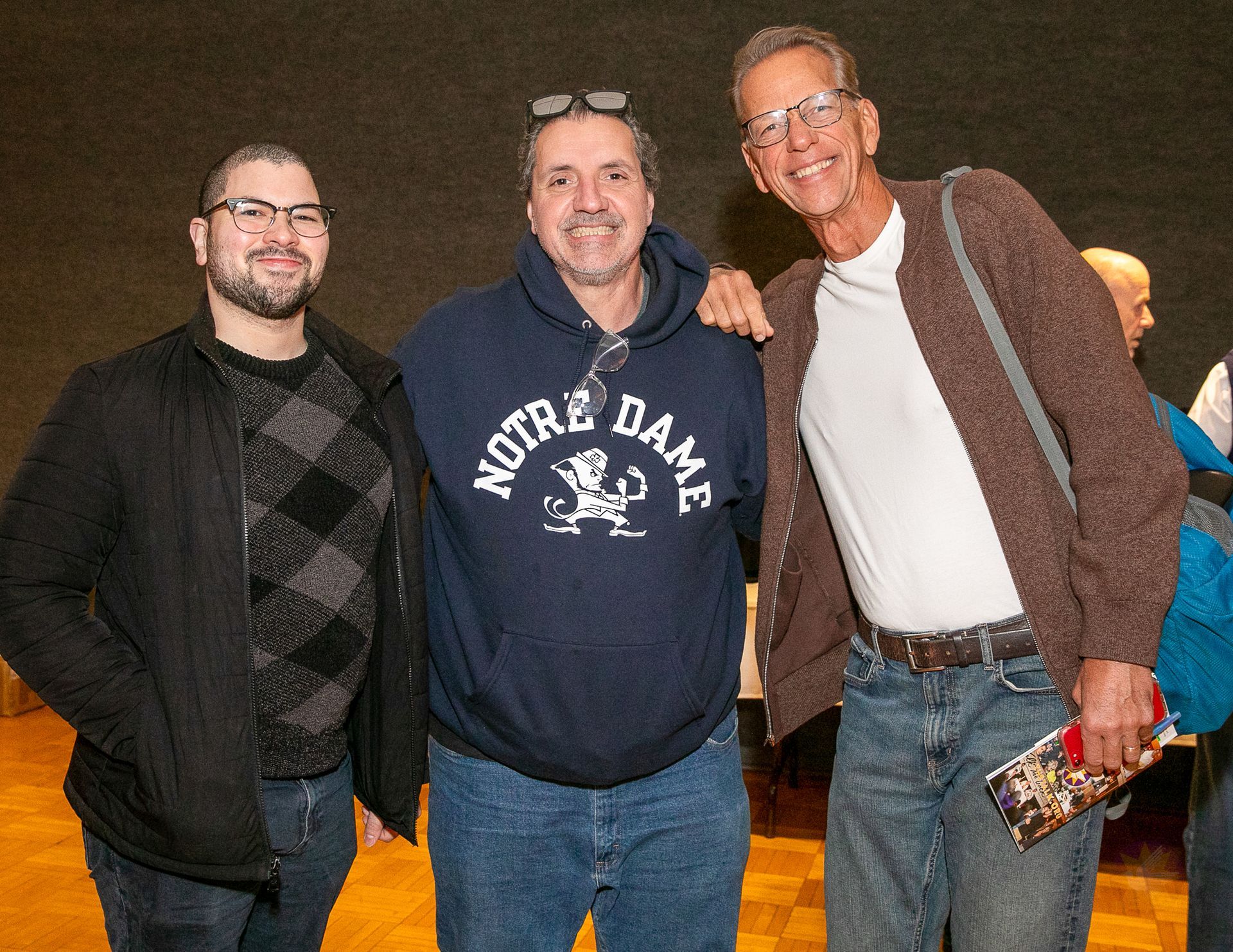 Three smiling people posing together at night, one wearing a Notre Dame sweatshirt.