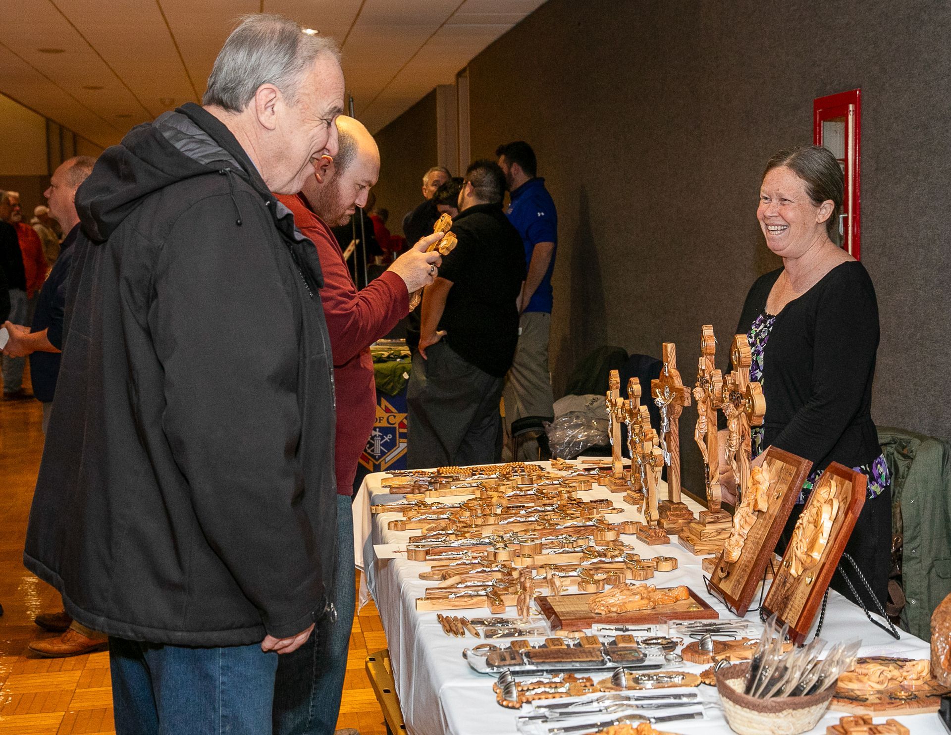 People browsing a craft vendor table at a Catholic men's conference, with handmade items displayed in rows.