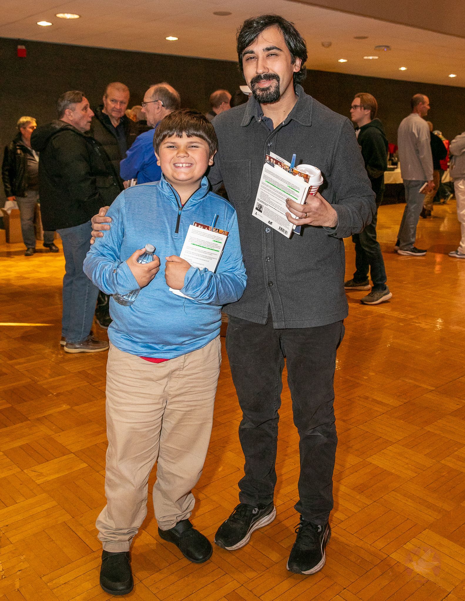 Two people standing together indoors, smiling, with event badges in a hall.