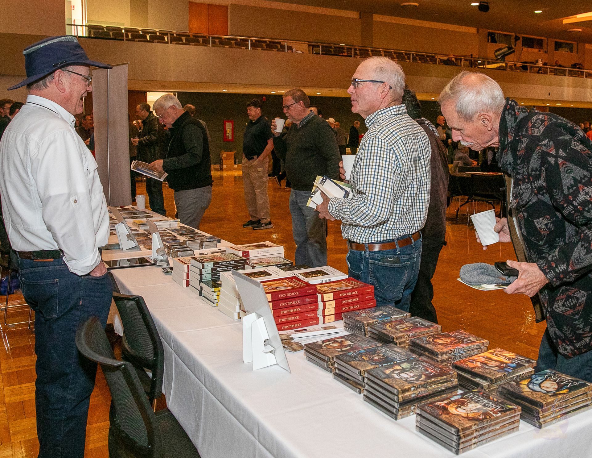 People browsing photo books at a vendor table in a convention hall