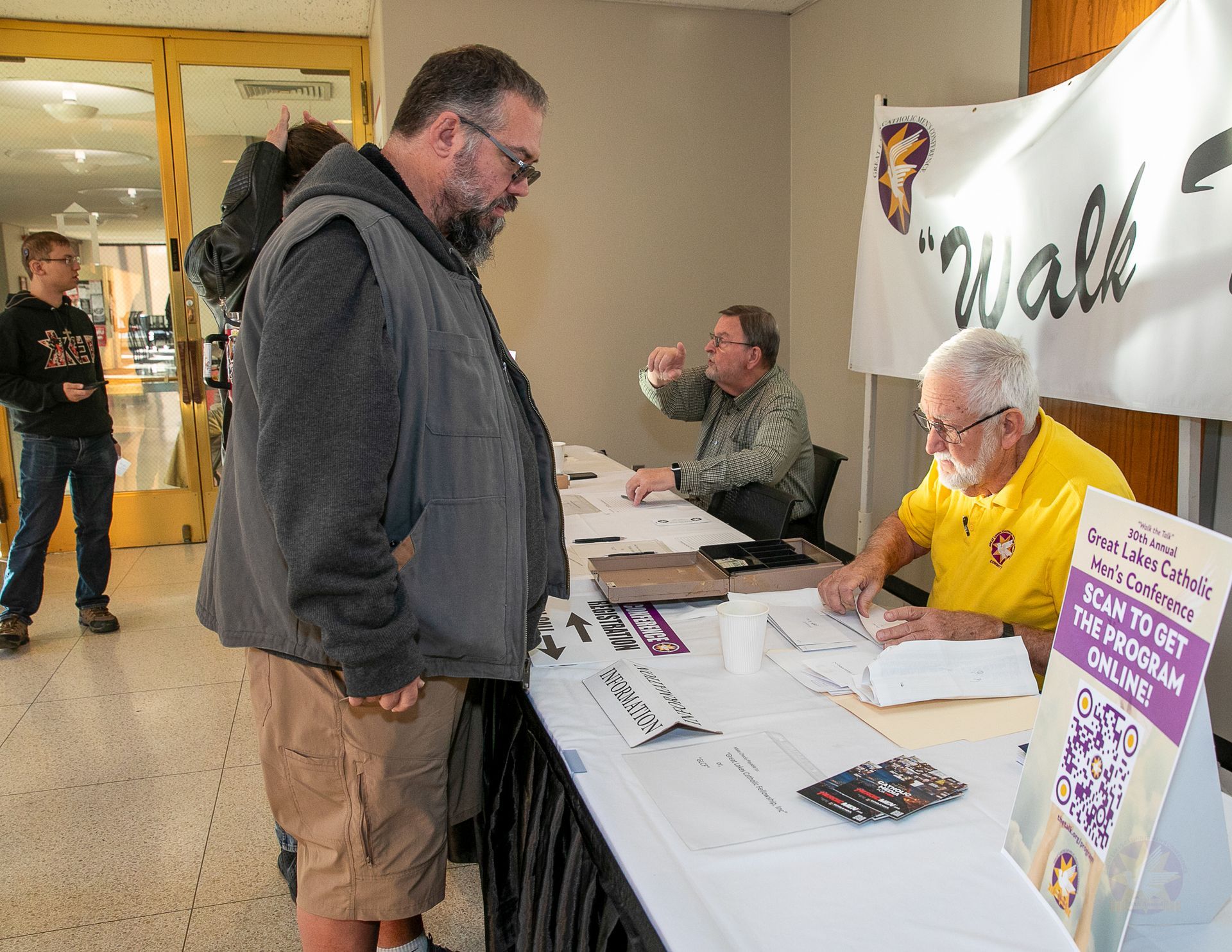 People at a registration table in a hallway, with volunteers and flyers on display