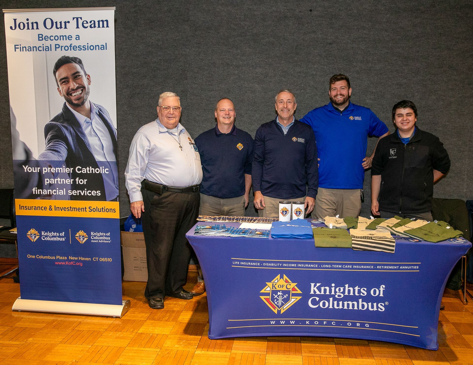 Five people stand behind a Knights of Columbus table and banner at a Catholic men's conference.