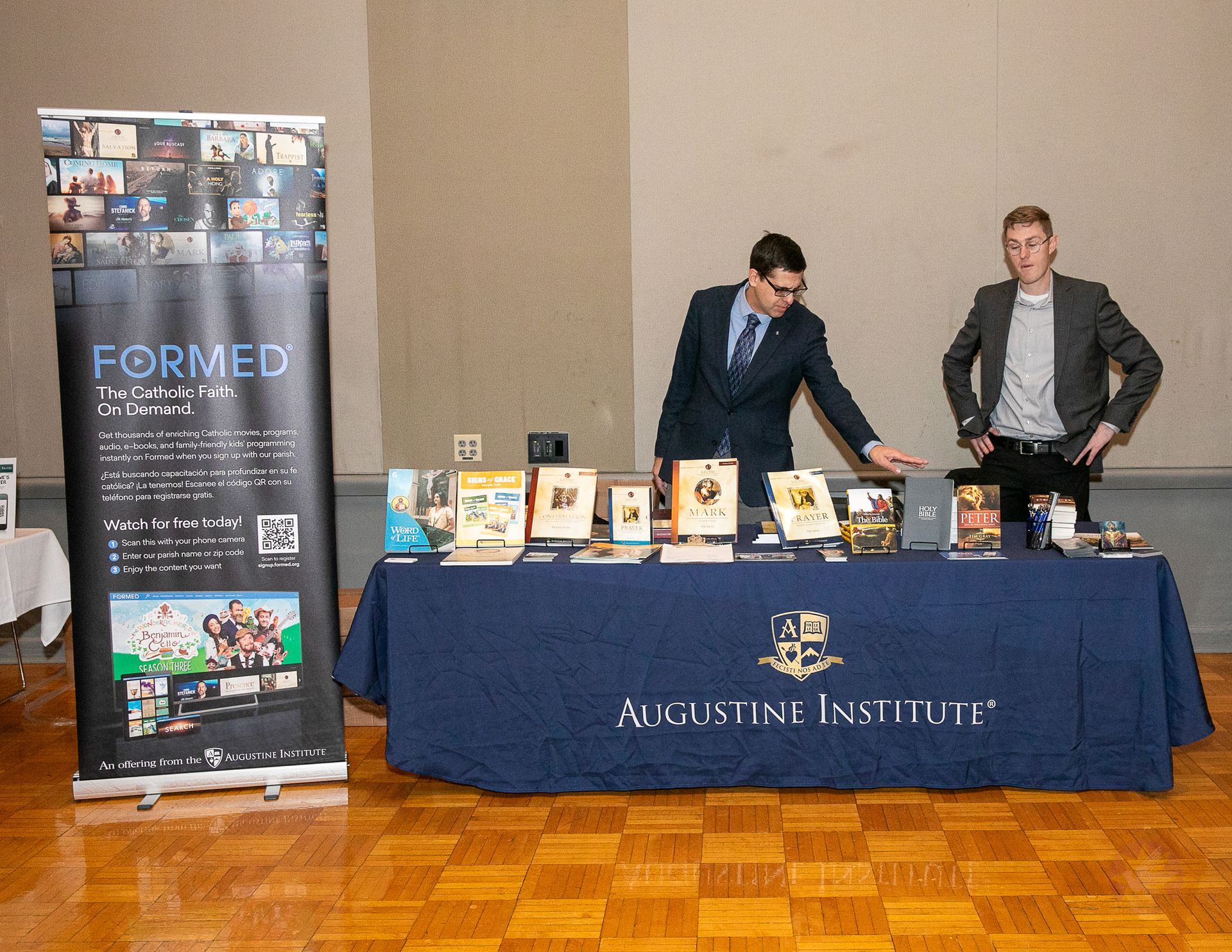Two men at a blue table display books at a conference booth beside a FORMED banner.