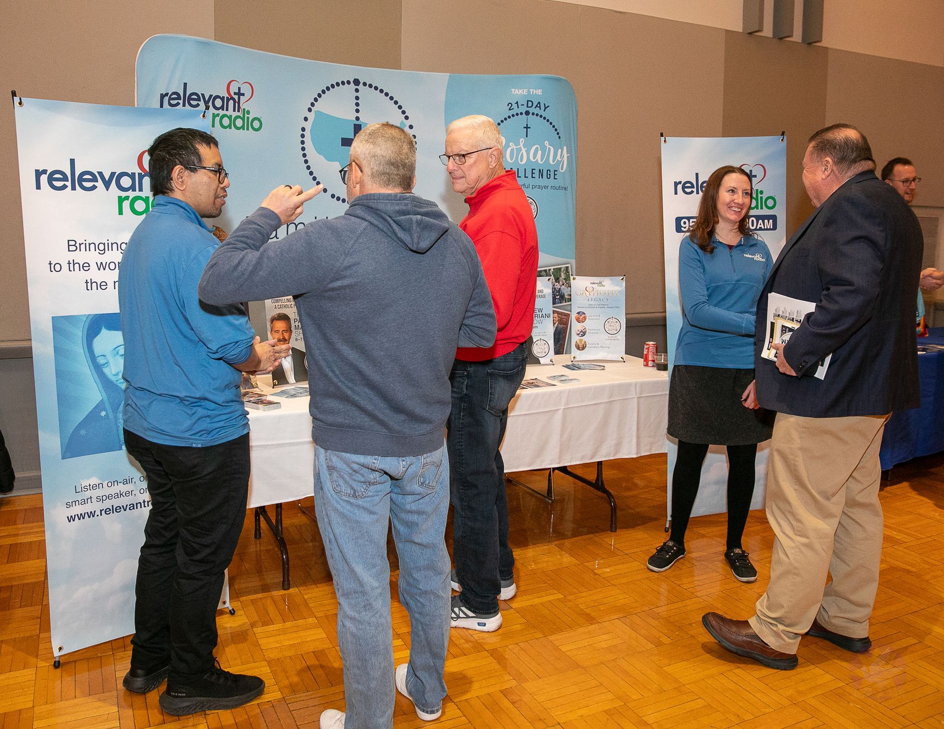 People chatting at a trade booth with banners, brochures, and tables at a Catholic men's conference.