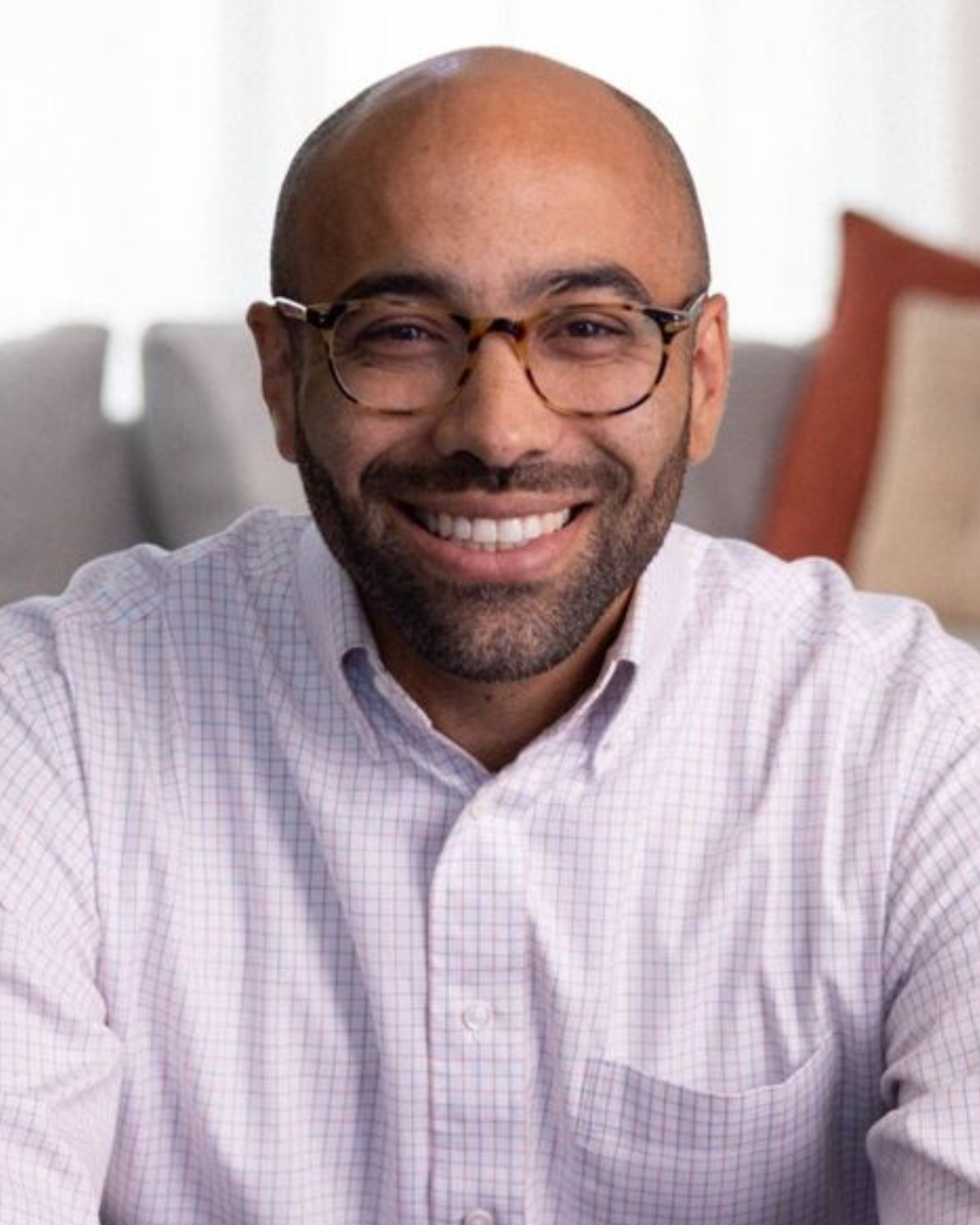 Portrait of Dr. Tim Gray smiling, wearing glasses, a blue shirt, and a gray blazer against a blurred green background