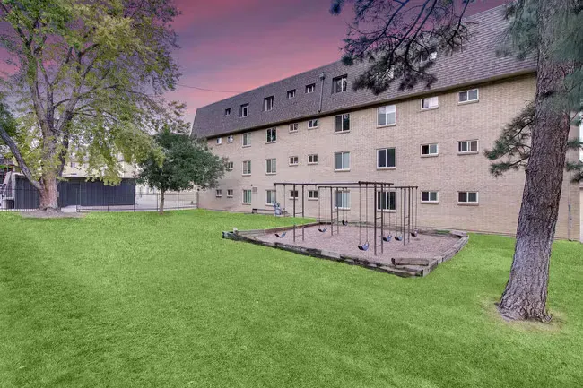 Apartment building with playground on green lawn under a purple and pink sky.