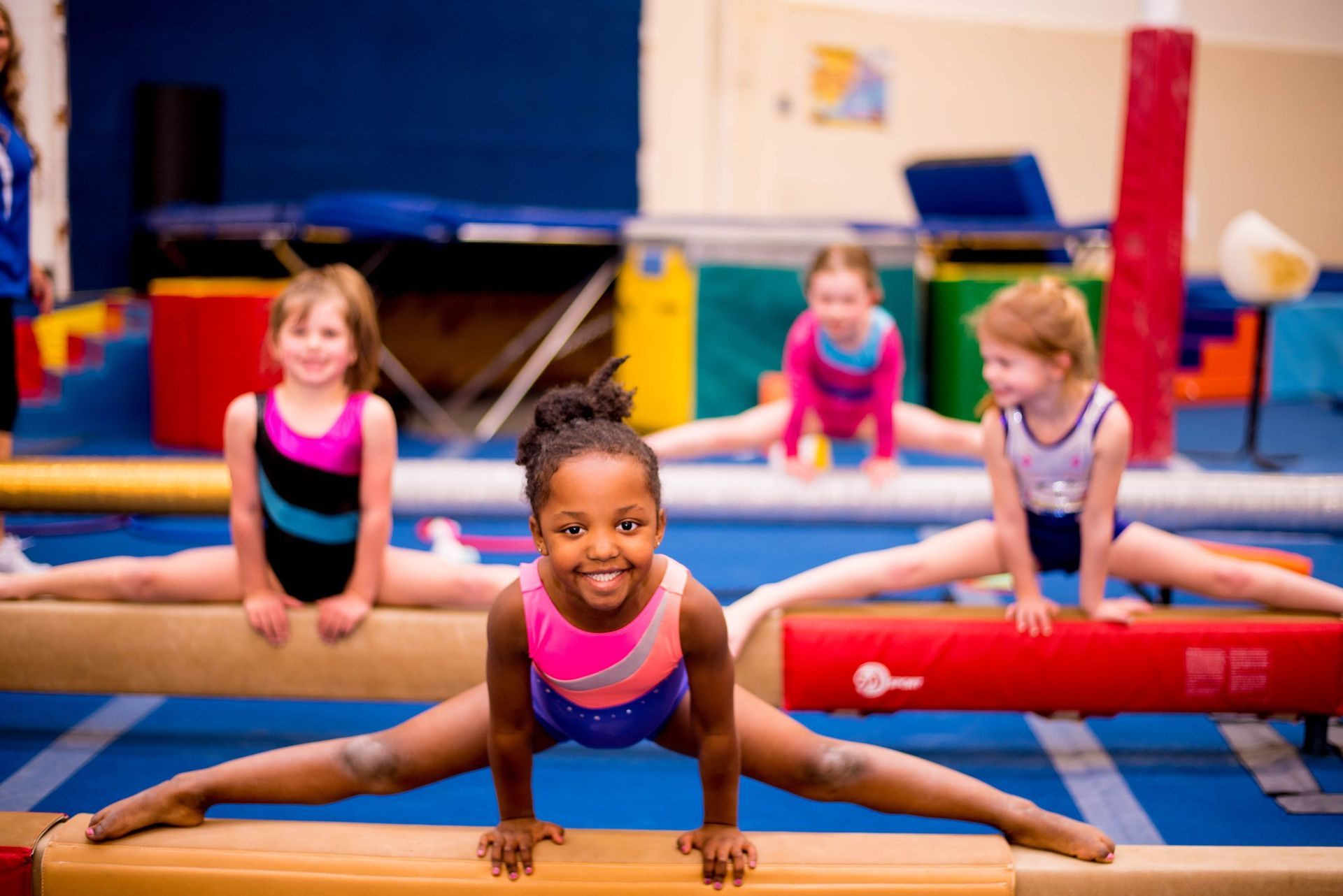 A group of young girls are doing exercises on a balance beam in a gym.
