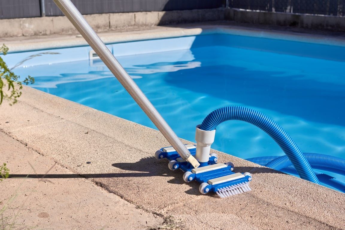 Pool vacuum head and hose on a concrete deck beside a blue swimming pool