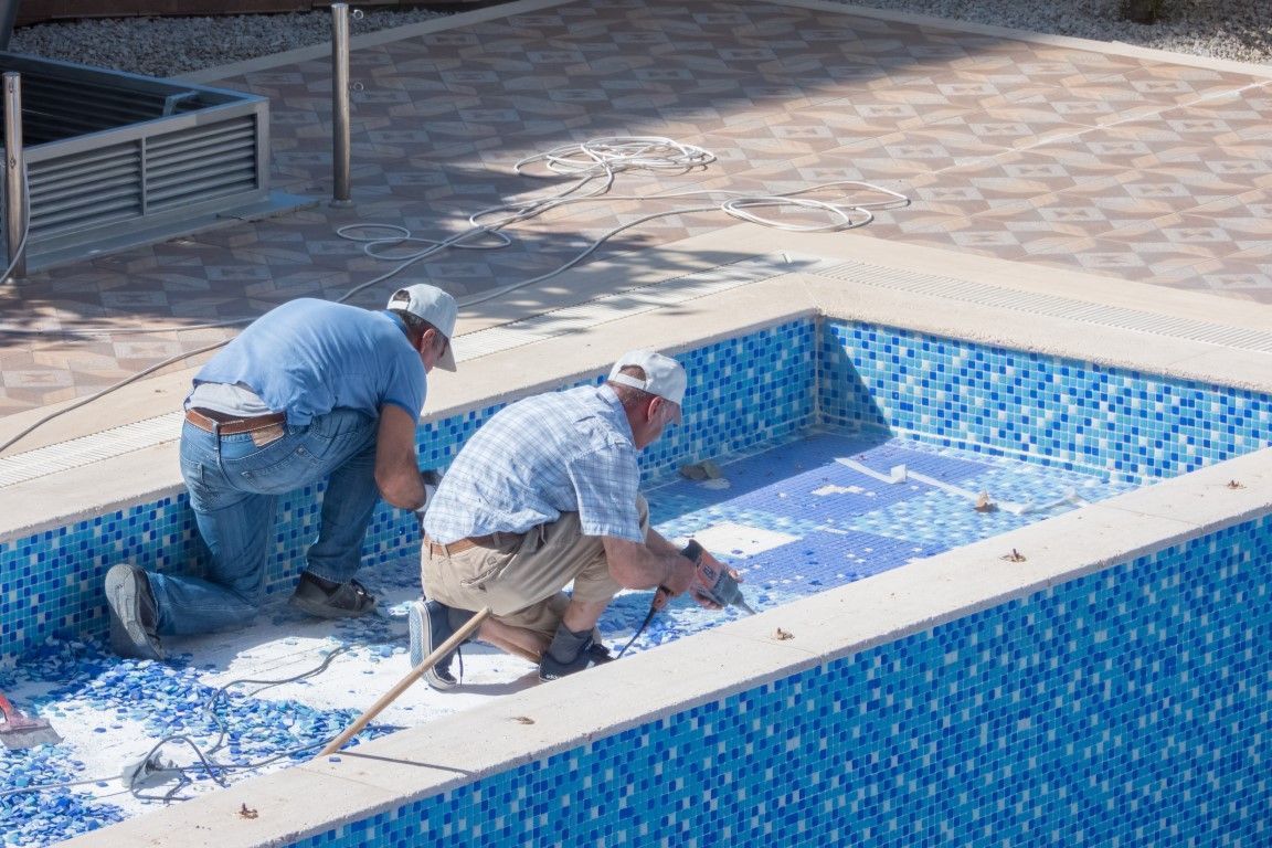 Two workers cleaning a blue-tiled empty pool with pressure washers
