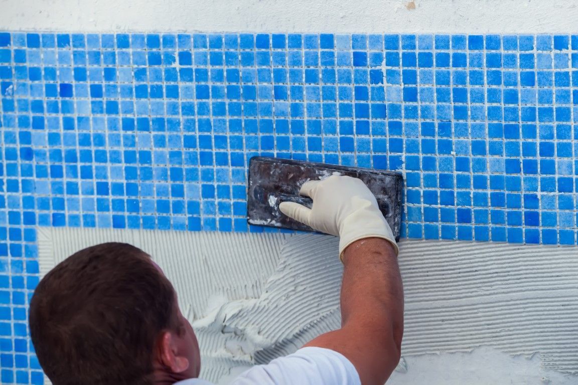 Worker plastering a blue tiled wall with a trowel