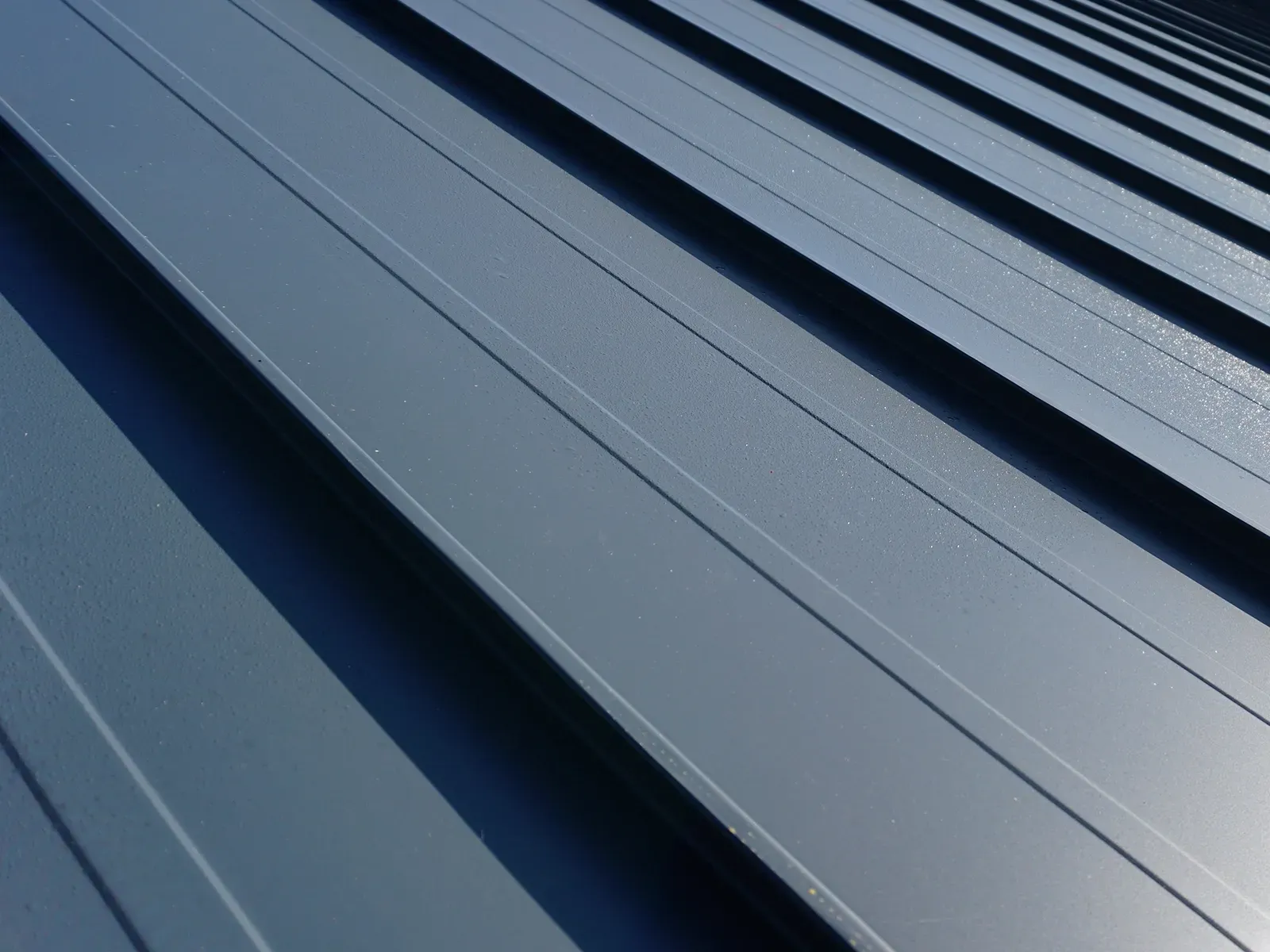 A close-up, angled view of a dark gray standing seam metal roof with repeating vertical ridges.