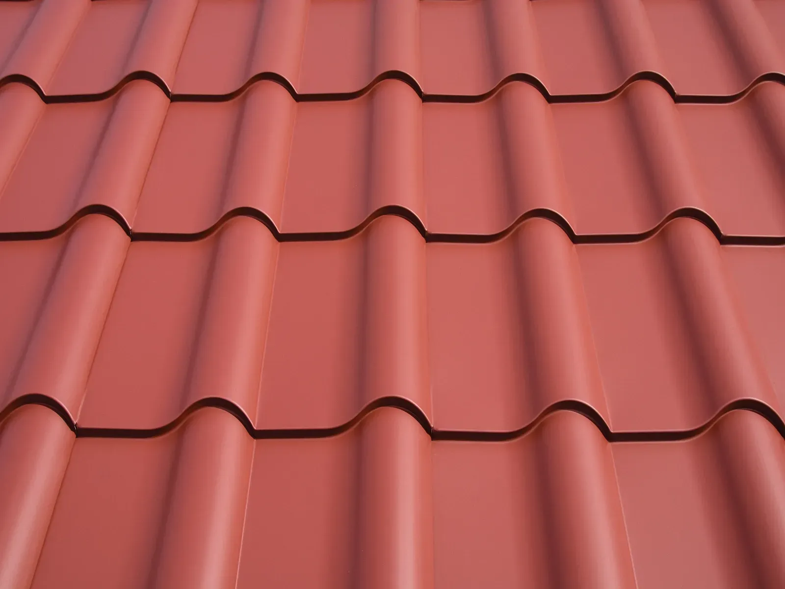 A close-up view of red, matte-finish metal roof tiles with a repeating curved profile.